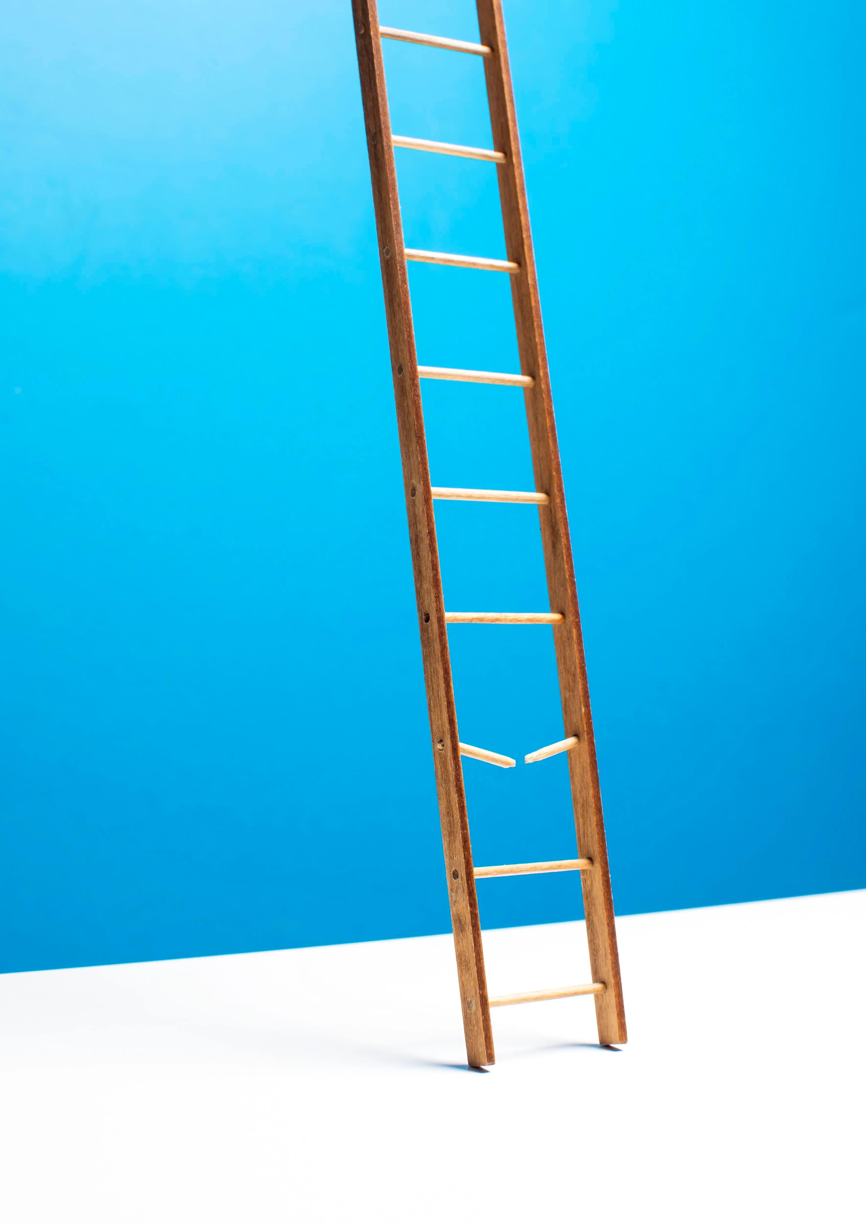 Ladder with broken rung against blue wall, illustrating the career progression gaps that AI has created by replacing traditional entry-level engineering roles