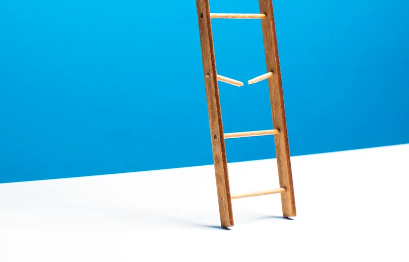 Ladder with broken rung against blue wall, illustrating the career progression gaps that AI has created by replacing traditional entry-level engineering roles
