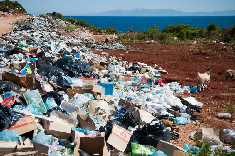 Massive landfill waste dump with plastic bottles and packaging scattered across landscape, showing environmental reality behind corporate green claims