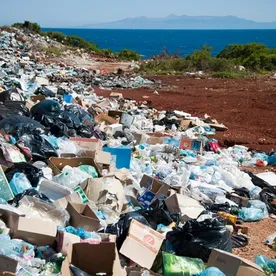 Massive landfill waste dump with plastic bottles and packaging scattered across landscape, showing environmental reality behind corporate green claims