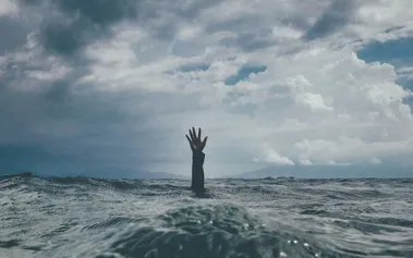 Hand reaching above rough ocean waves, representing the subtle burnout warning signs employees send that leaders often overlook