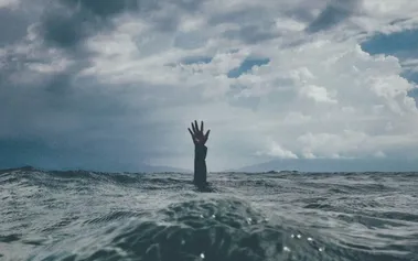 Hand reaching above rough ocean waves, representing the subtle burnout warning signs employees send that leaders often overlook