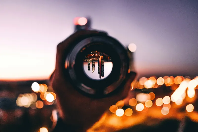 Hand holding a lens showing an inverted cityscape with blurred lights in background, illustrating how founder vision can both focus and limit team perspective