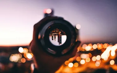 Hand holding a lens showing an inverted cityscape with blurred lights in background, illustrating how founder vision can both focus and limit team perspective
