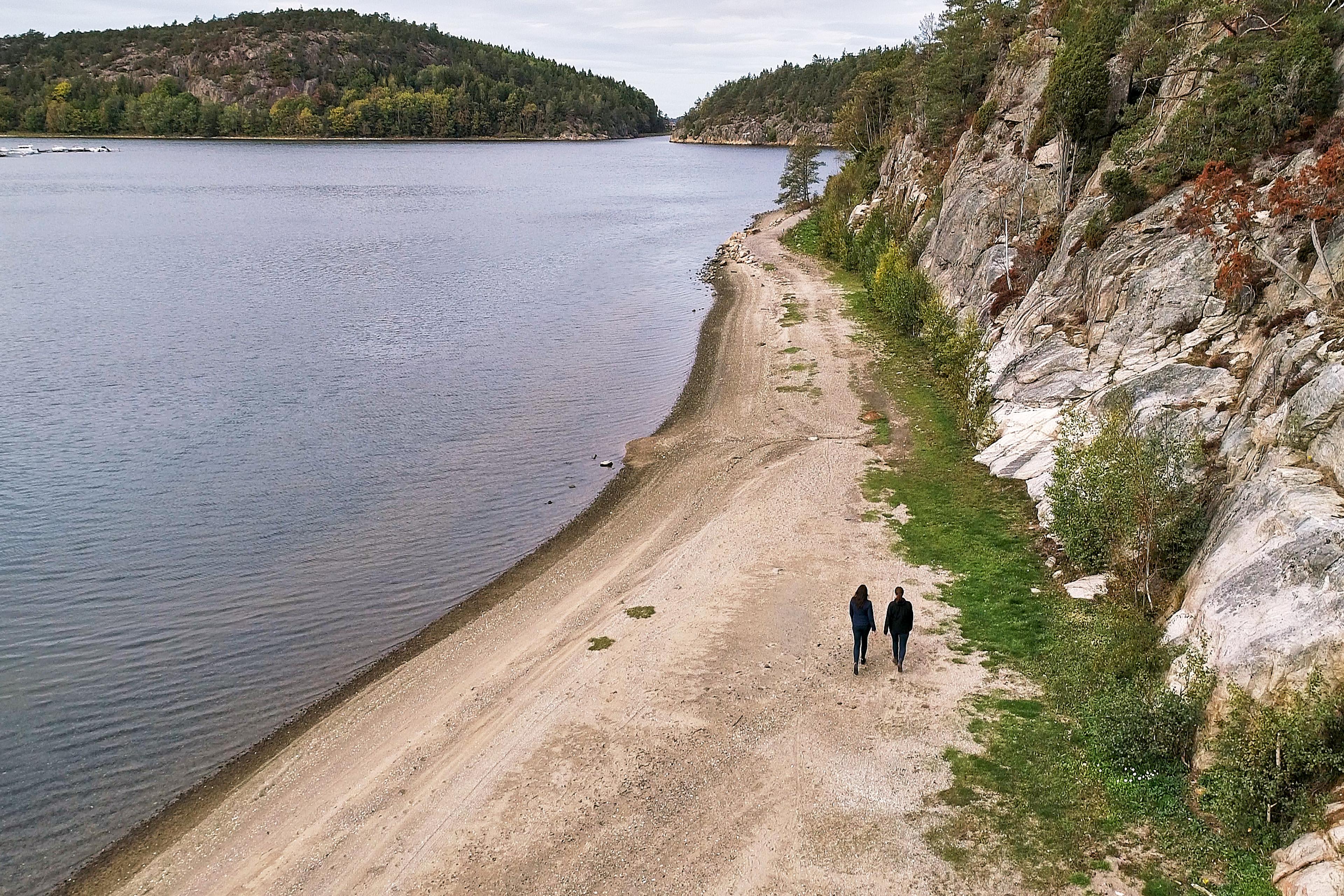 Två personer som promenerar i naturen på Daftö Resort, på strand med havet och bohuslänska klippor på var sida.