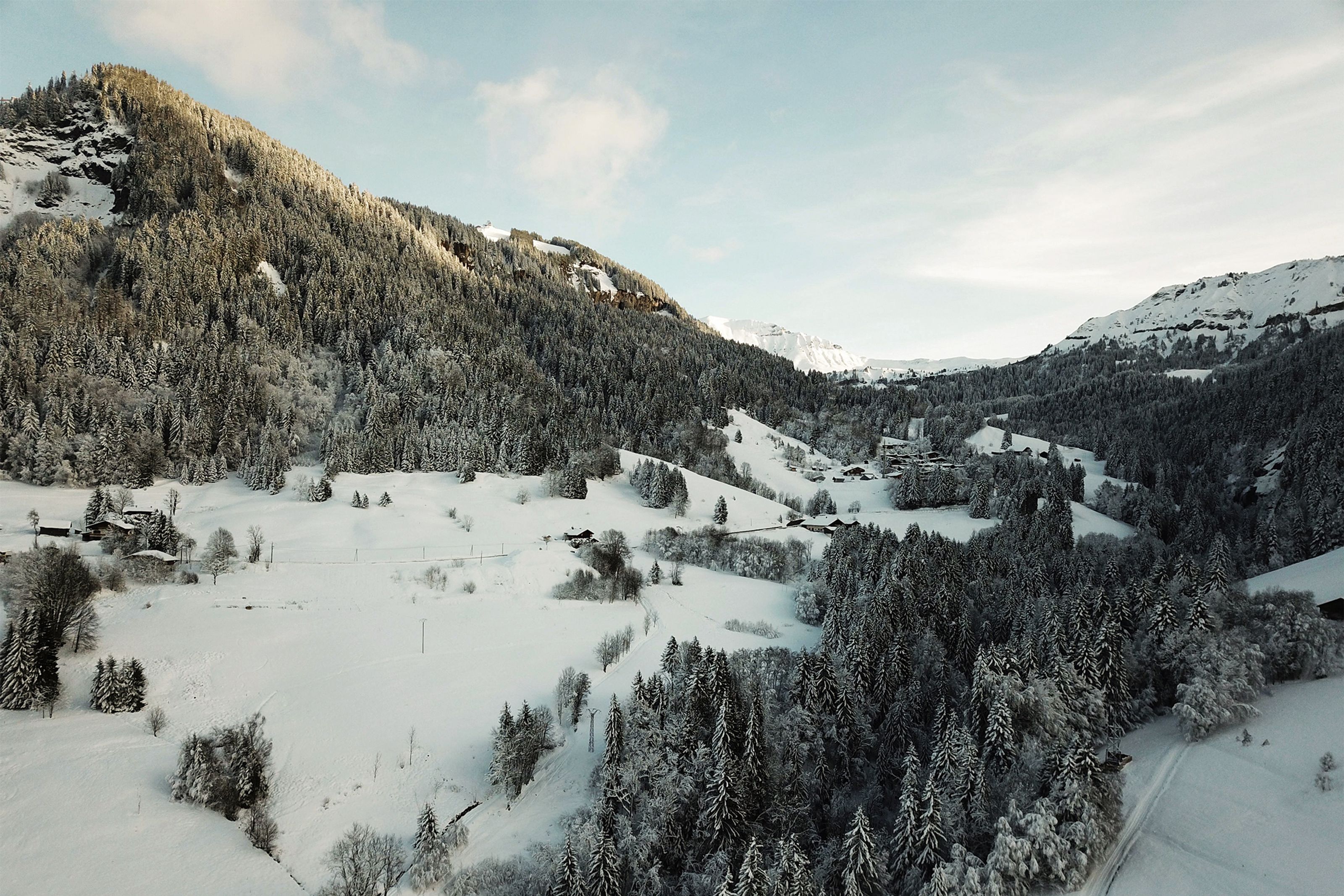 Snow-covered mountain valley with evergreen forests and distant chalets.