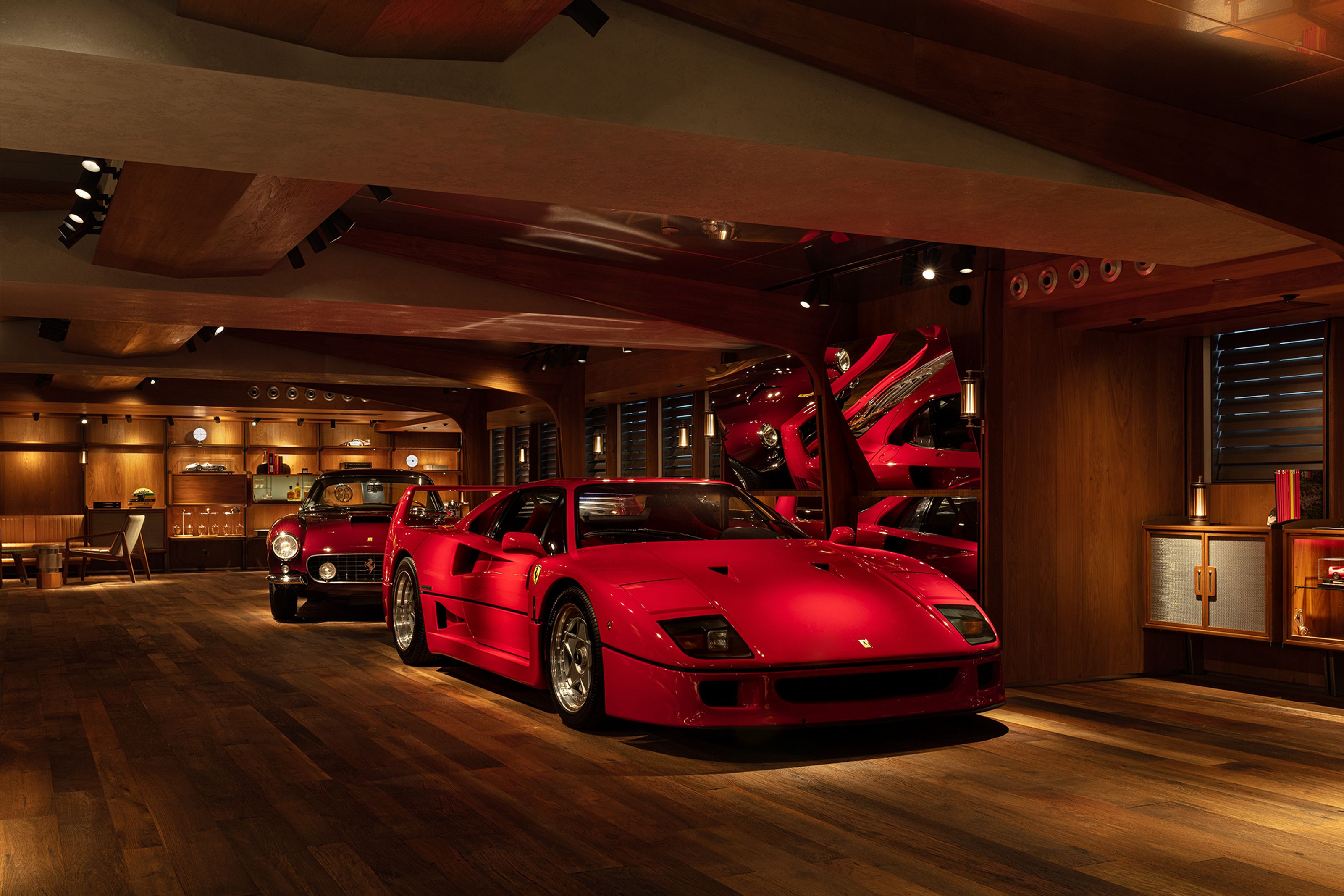 A red Ferrari F40 and a classic red Ferrari in a luxurious, wood-finished garage.