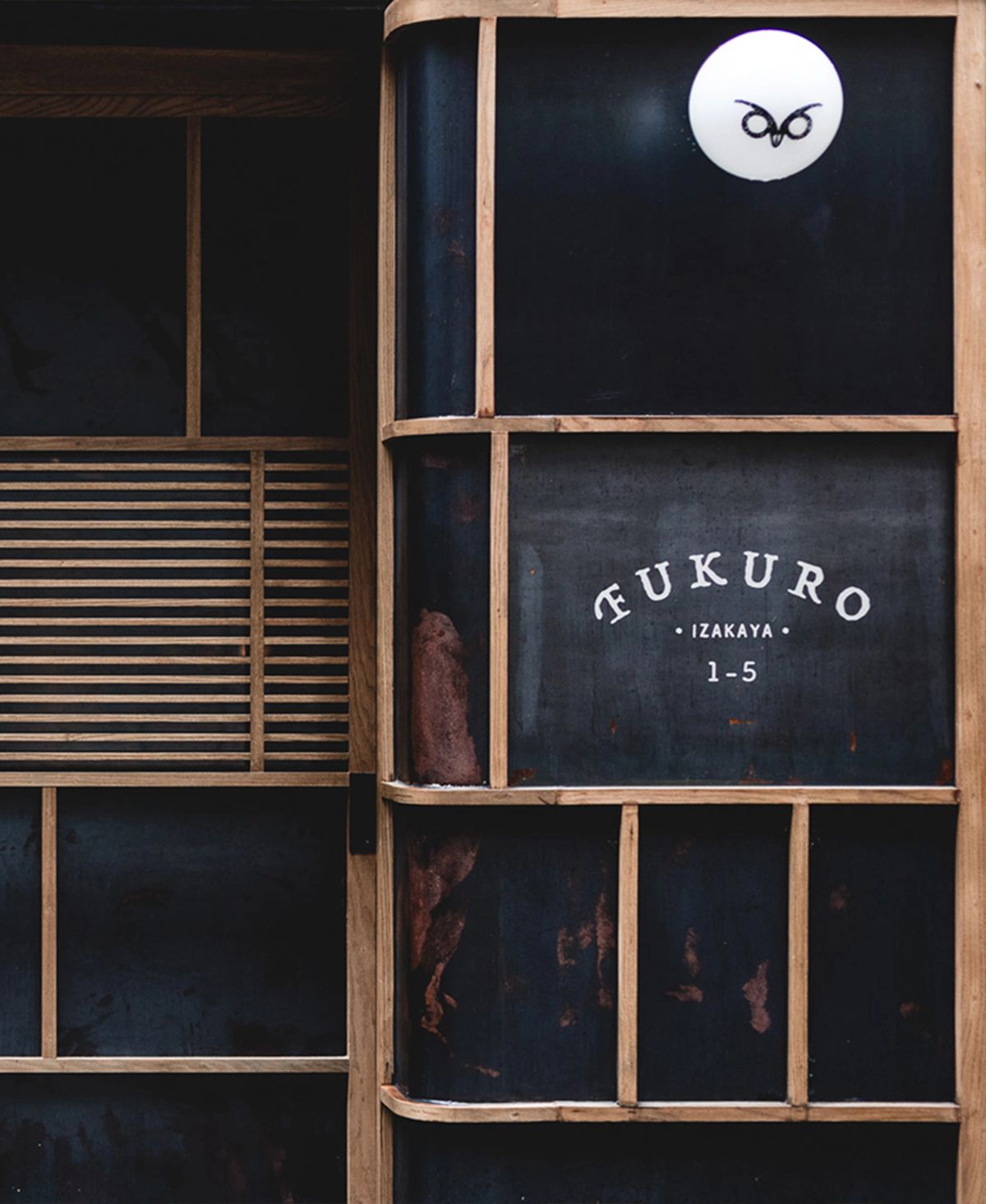 Dark, wooden-framed storefront sign for FUKURO IZAKAYA, featuring an owl logo.