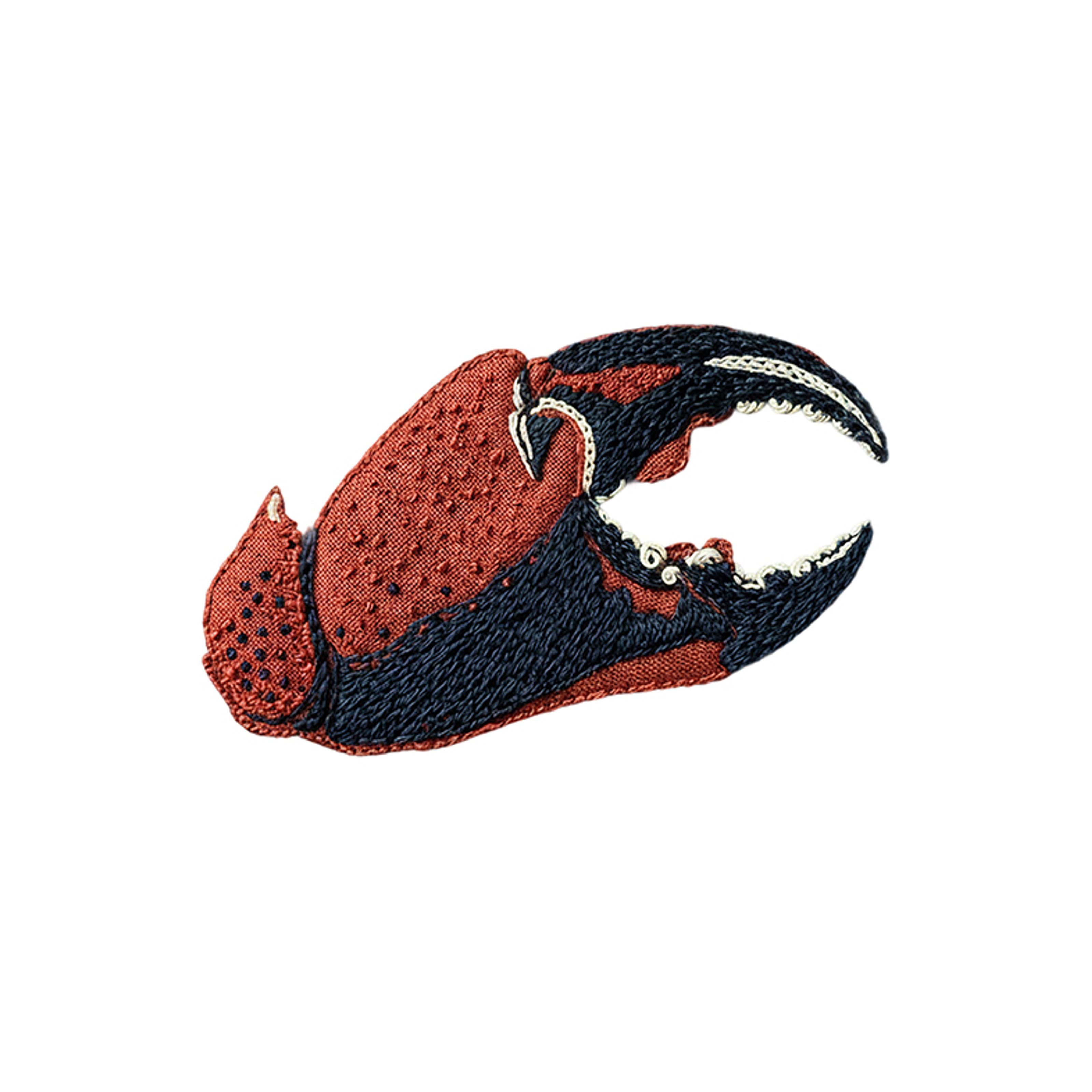 Embroidered crab claw in red-orange, dark blue, and white.