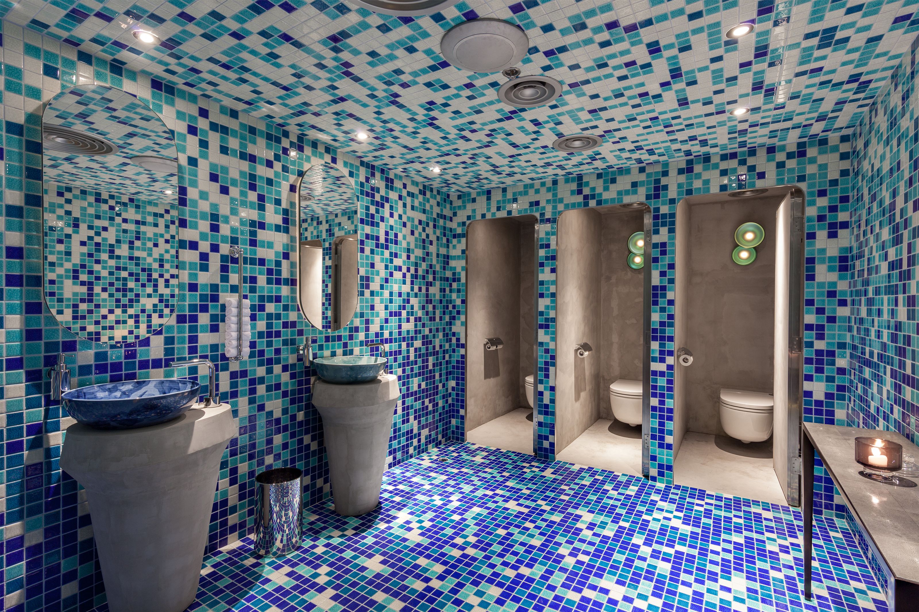 Blue and white mosaic tiled restroom with two sinks and three toilet stalls.