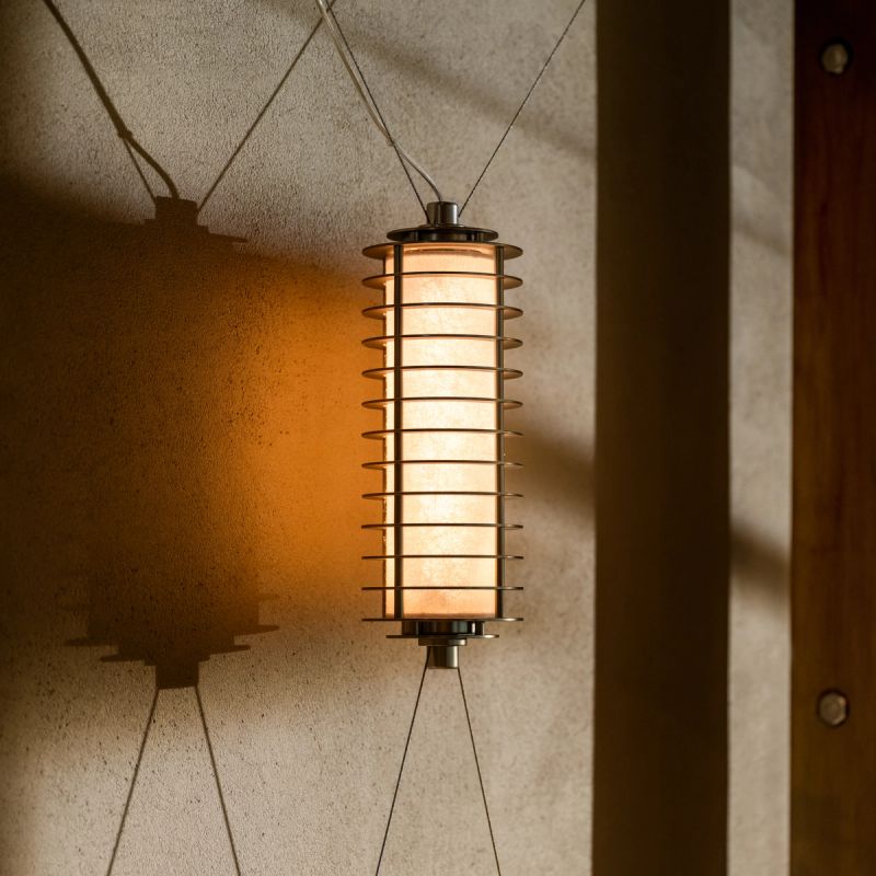 A lit modern rectangular lantern-style lamp hangs against a textured wall, casting shadows.