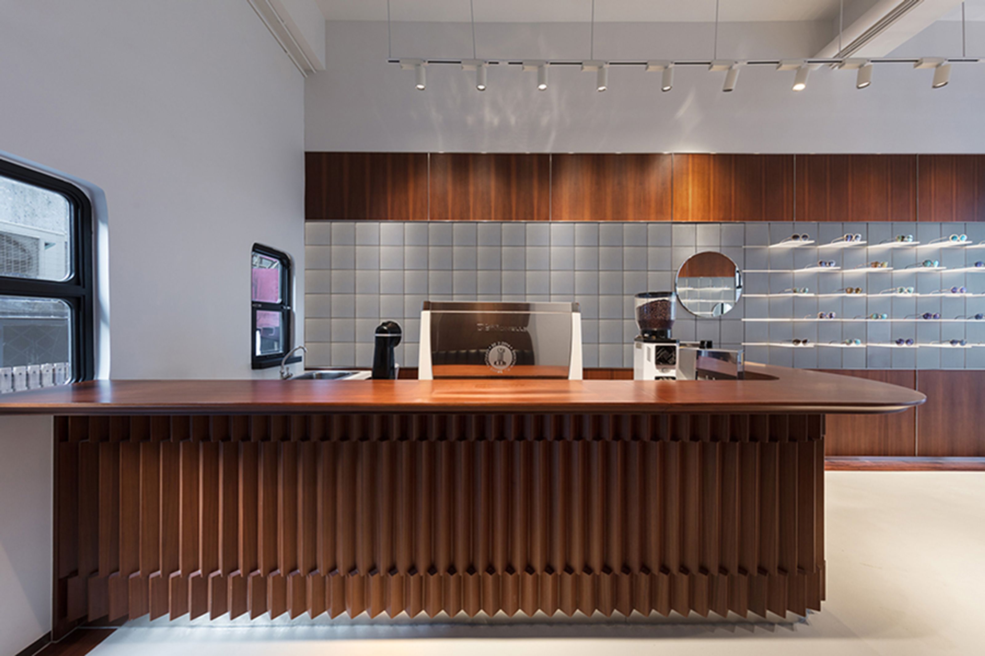 Modern eyewear shop interior with a dark wooden counter, coffee equipment, and wall displays of eyeglasses.
