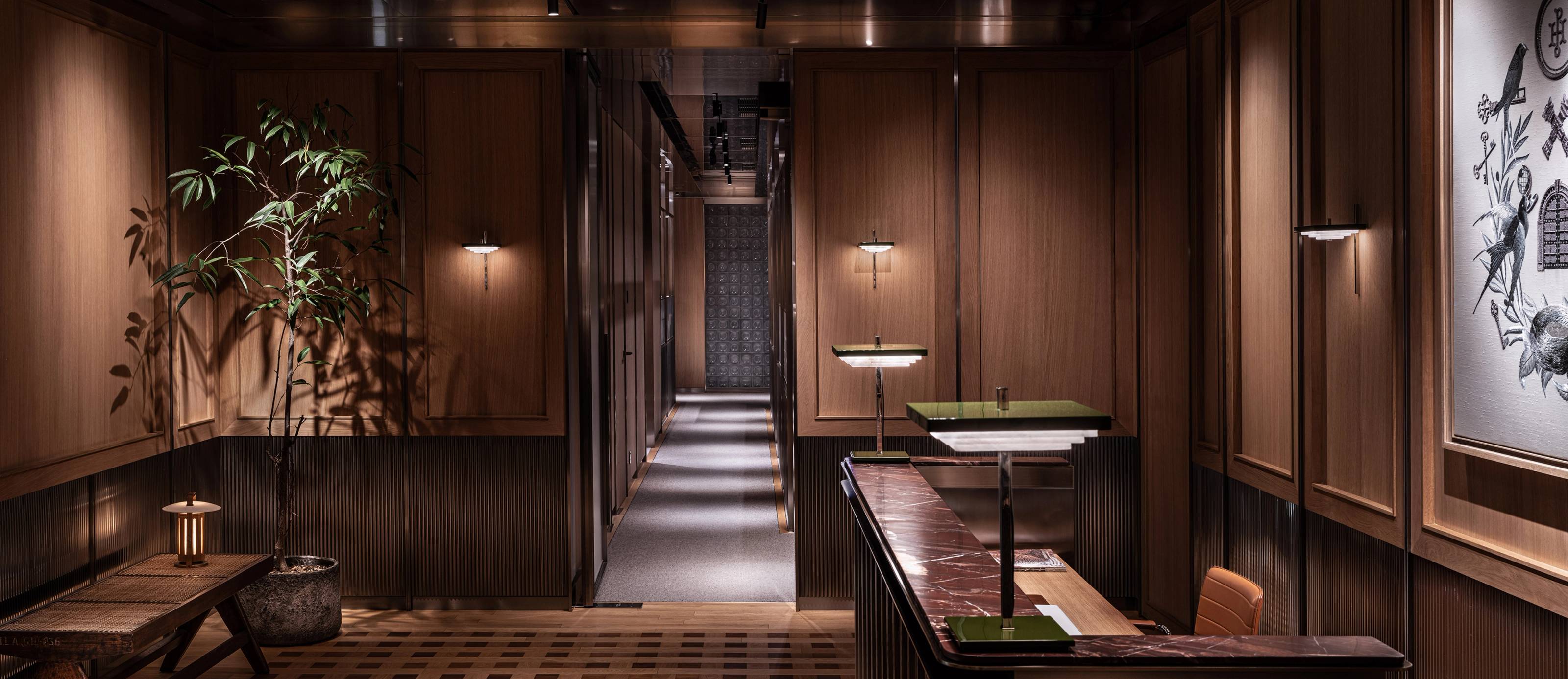 A warm, wood-paneled reception area with a marble-topped desk, a potted plant, and a long hallway.