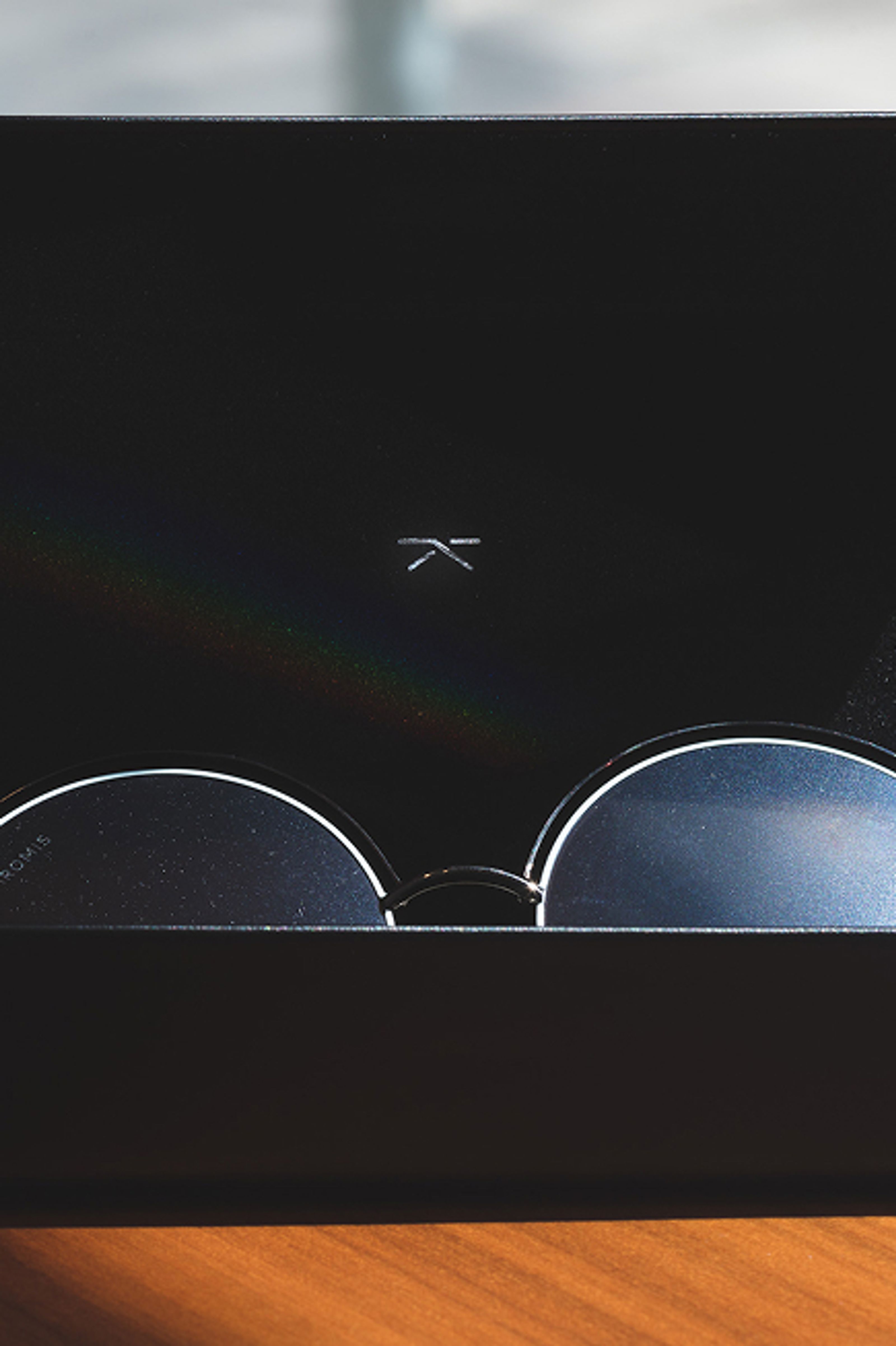 Black sunglasses with "CHROMIS" on the lens, in a black case with a K logo and a rainbow reflection.