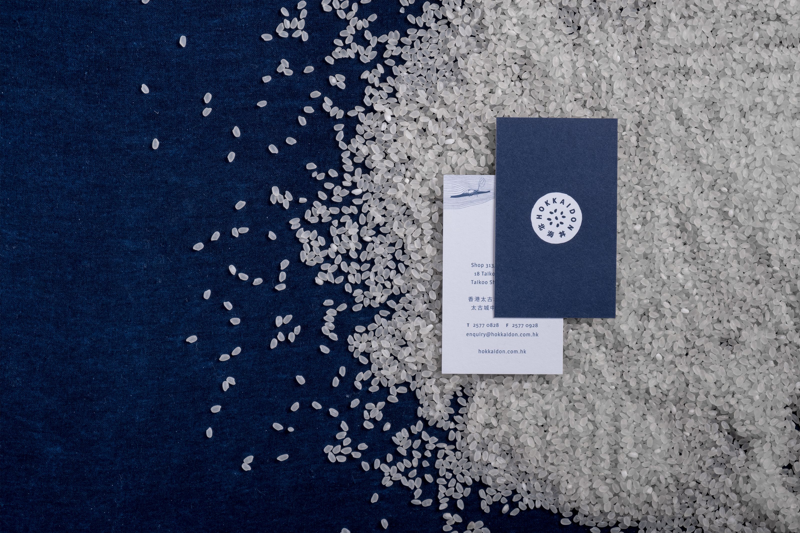 Dark blue and white business cards on a dark blue surface with scattered white rice.