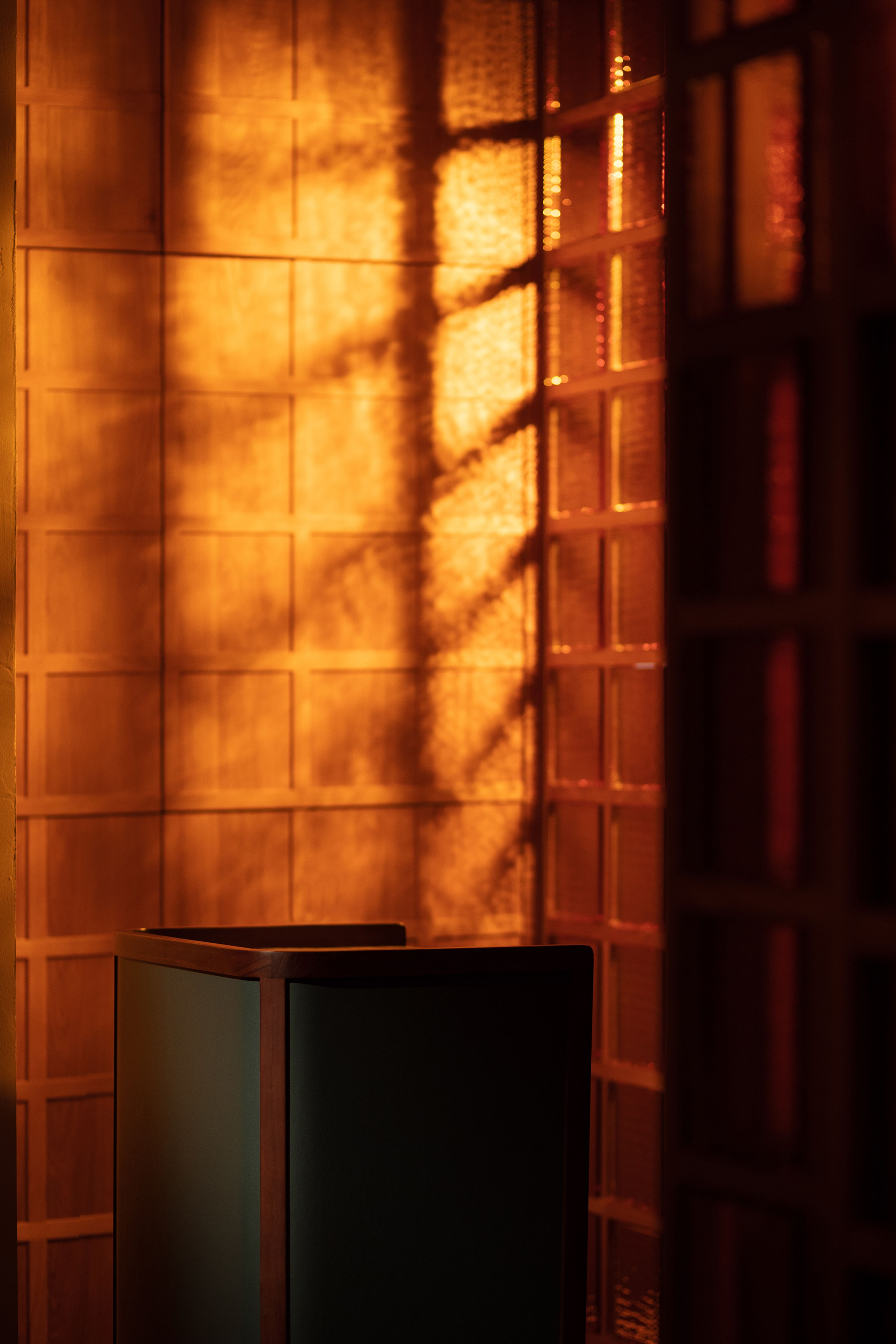Warm orange light and window shadows on grid-patterned walls, with a dark lectern in the foreground.
