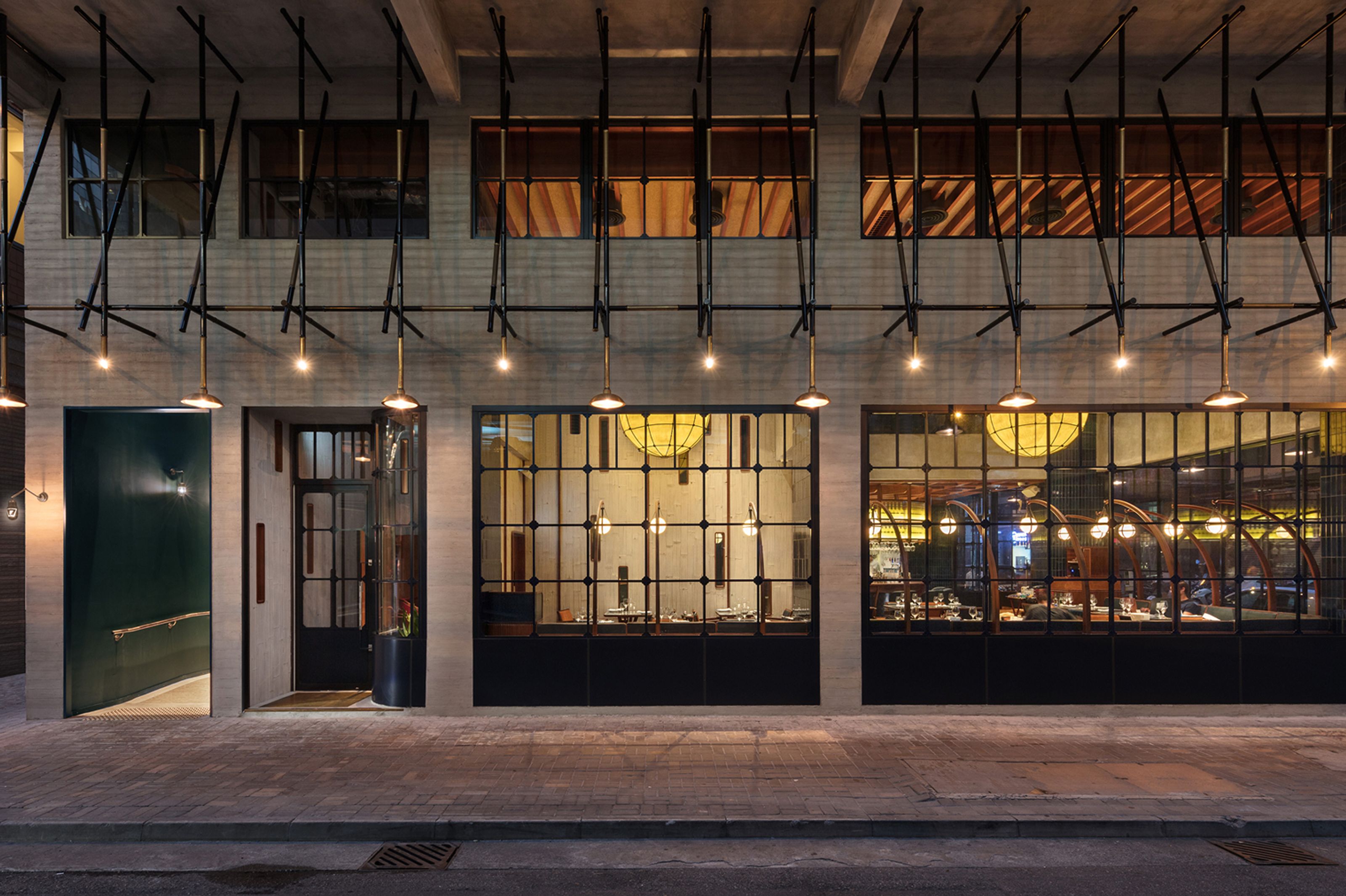 Modern restaurant exterior at night with large grid windows, illuminated interior, and decorative hanging lights.