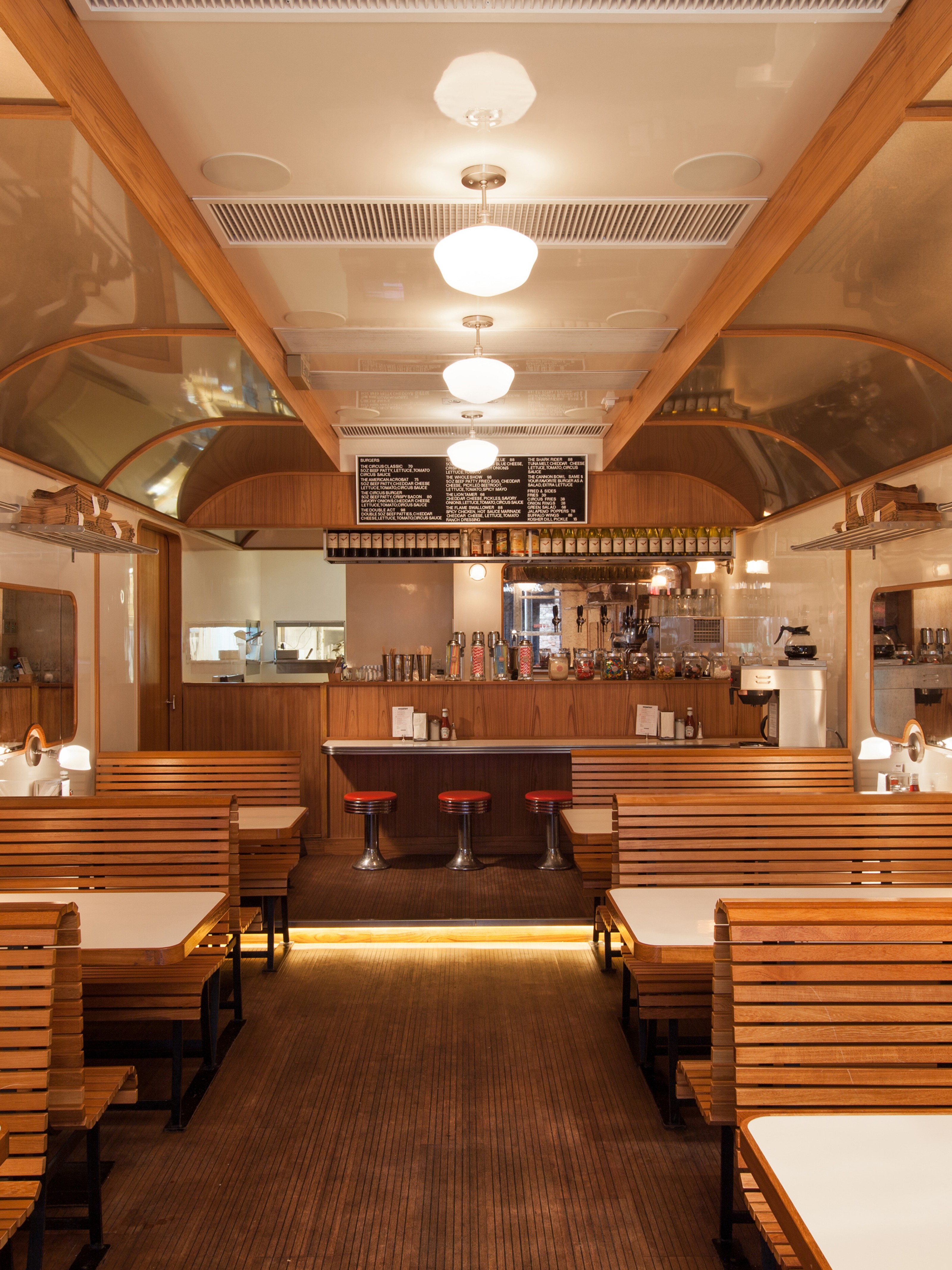 A retro diner interior resembling a train car, with wooden slatted booths, a central aisle, and a counter with red bar stools.