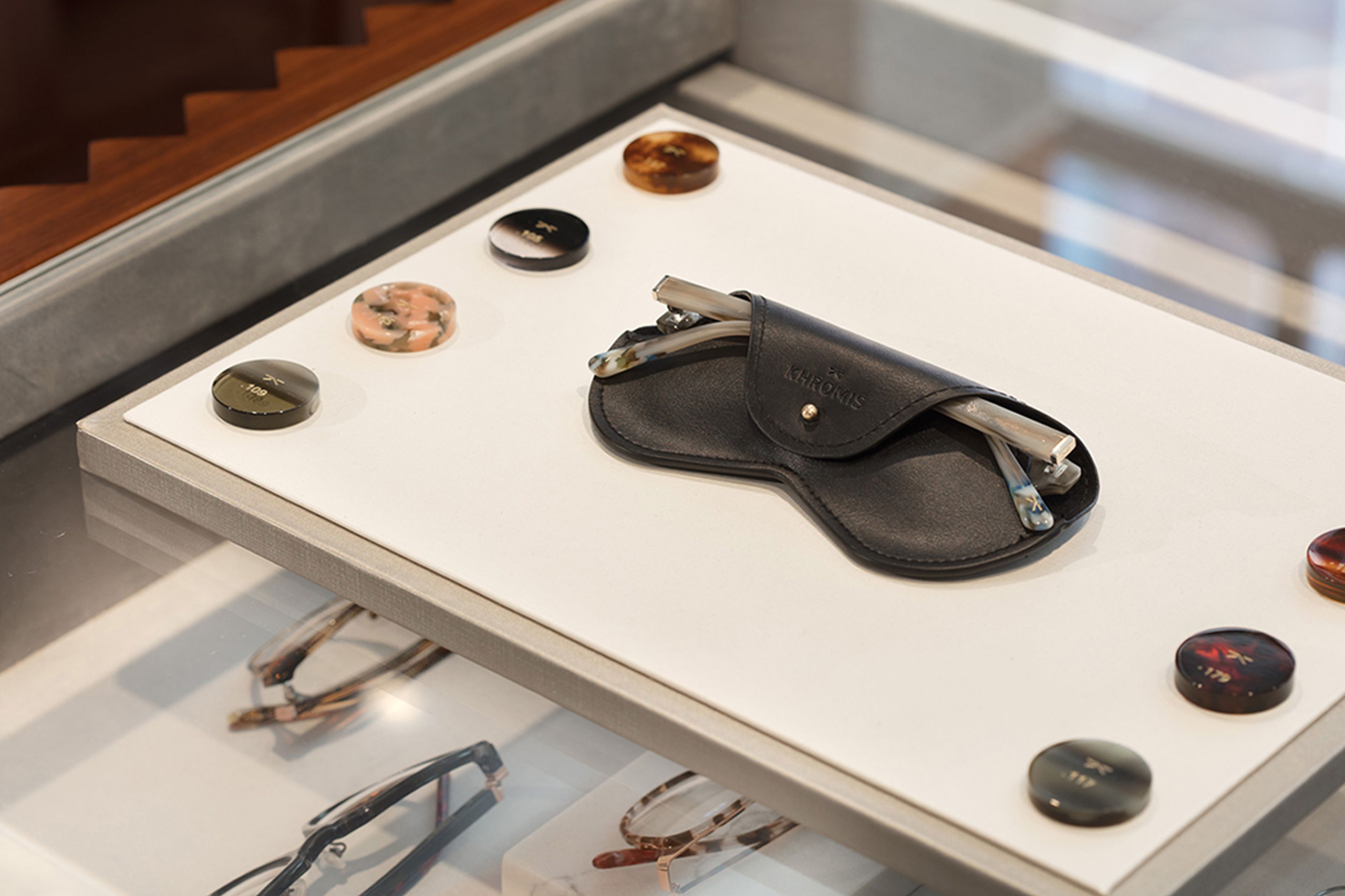Eyeglasses in a black leather case on a white display surface, surrounded by colorful samples.