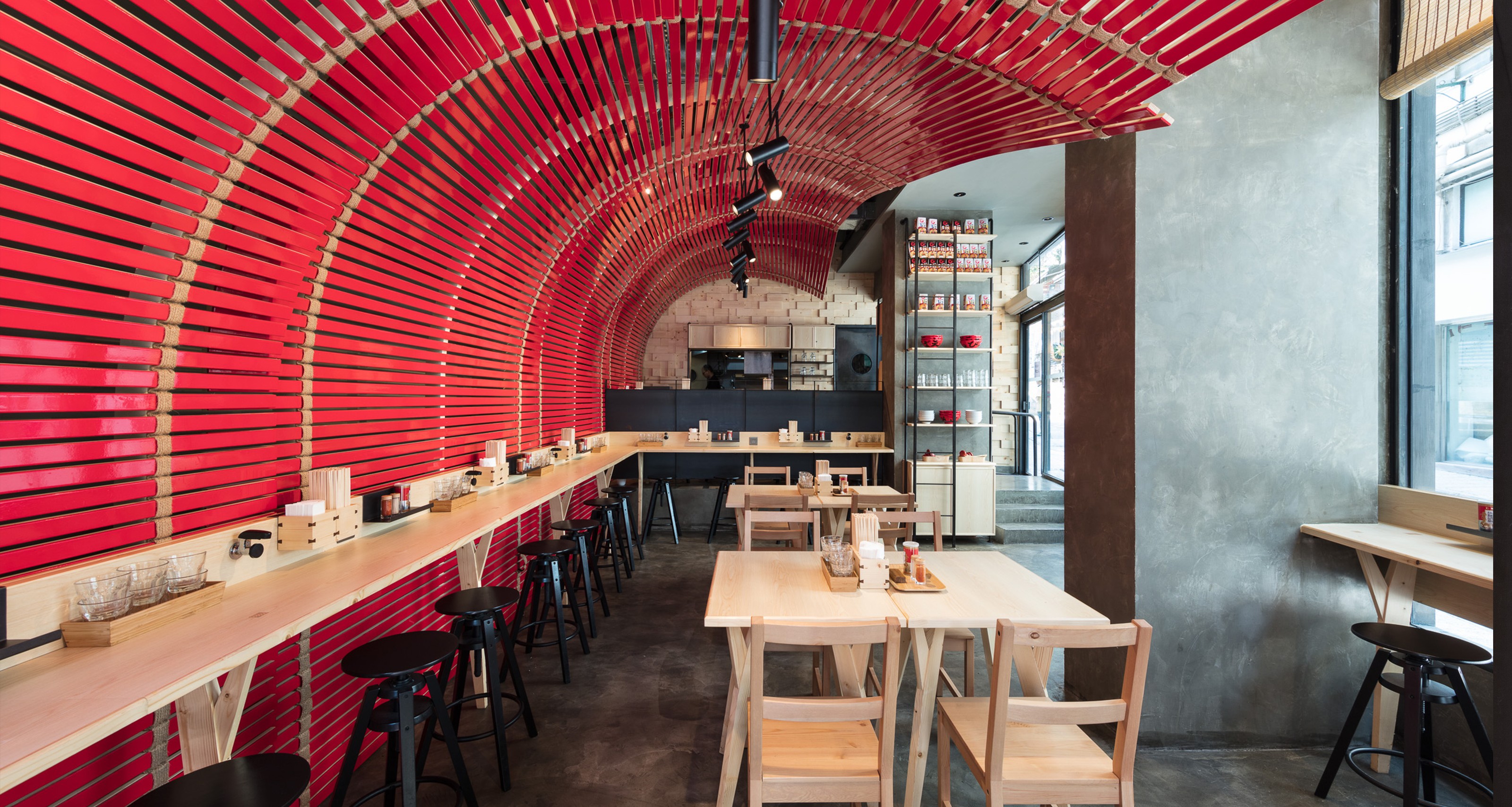 Modern restaurant with an arched red slatted ceiling and wall, light wood counters, and tables.