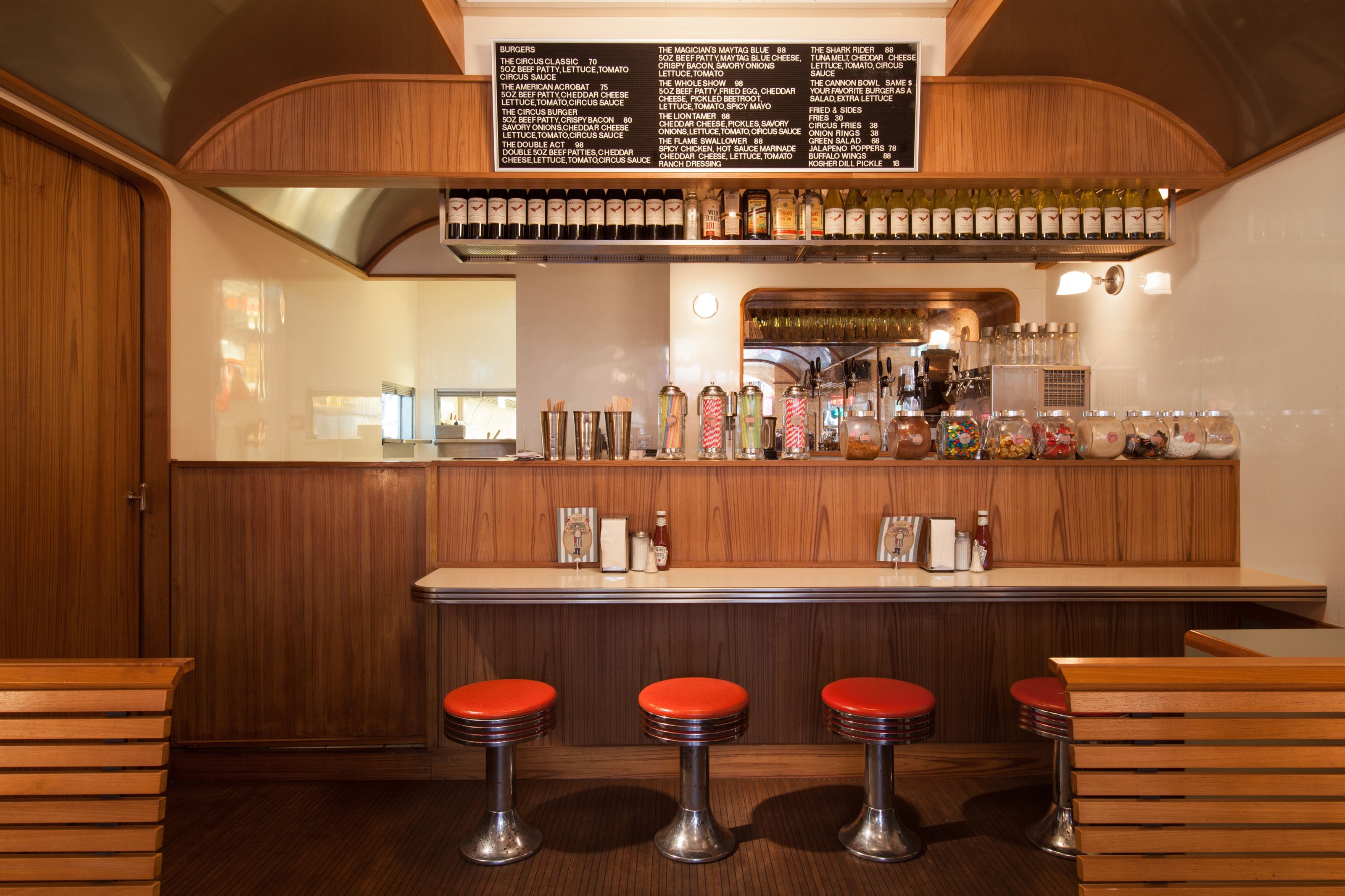 Retro diner interior with wood paneling, a counter with red stools, and a menu board.