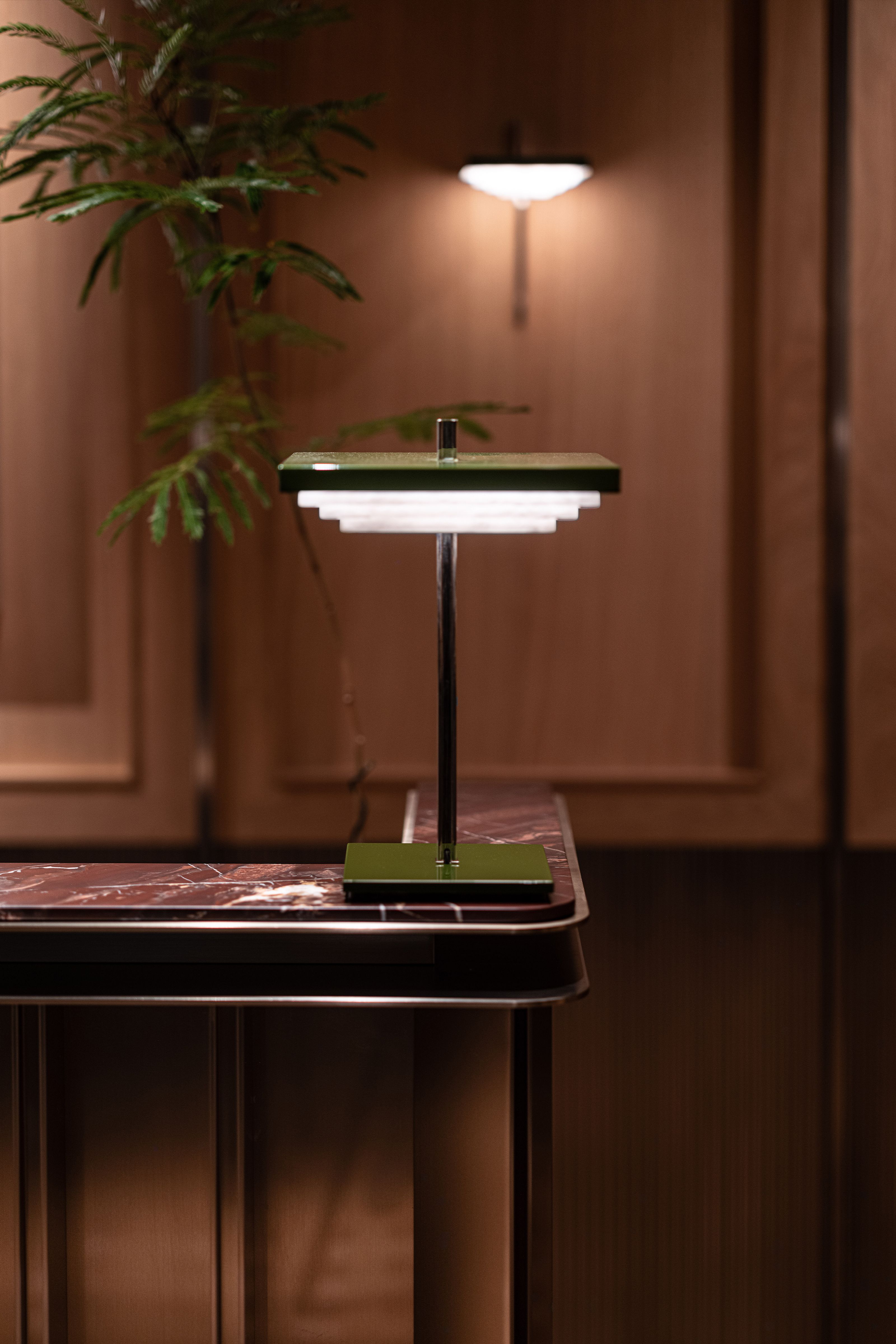 Art Deco-style green and metal table lamp with tiered light on a dark marble counter.