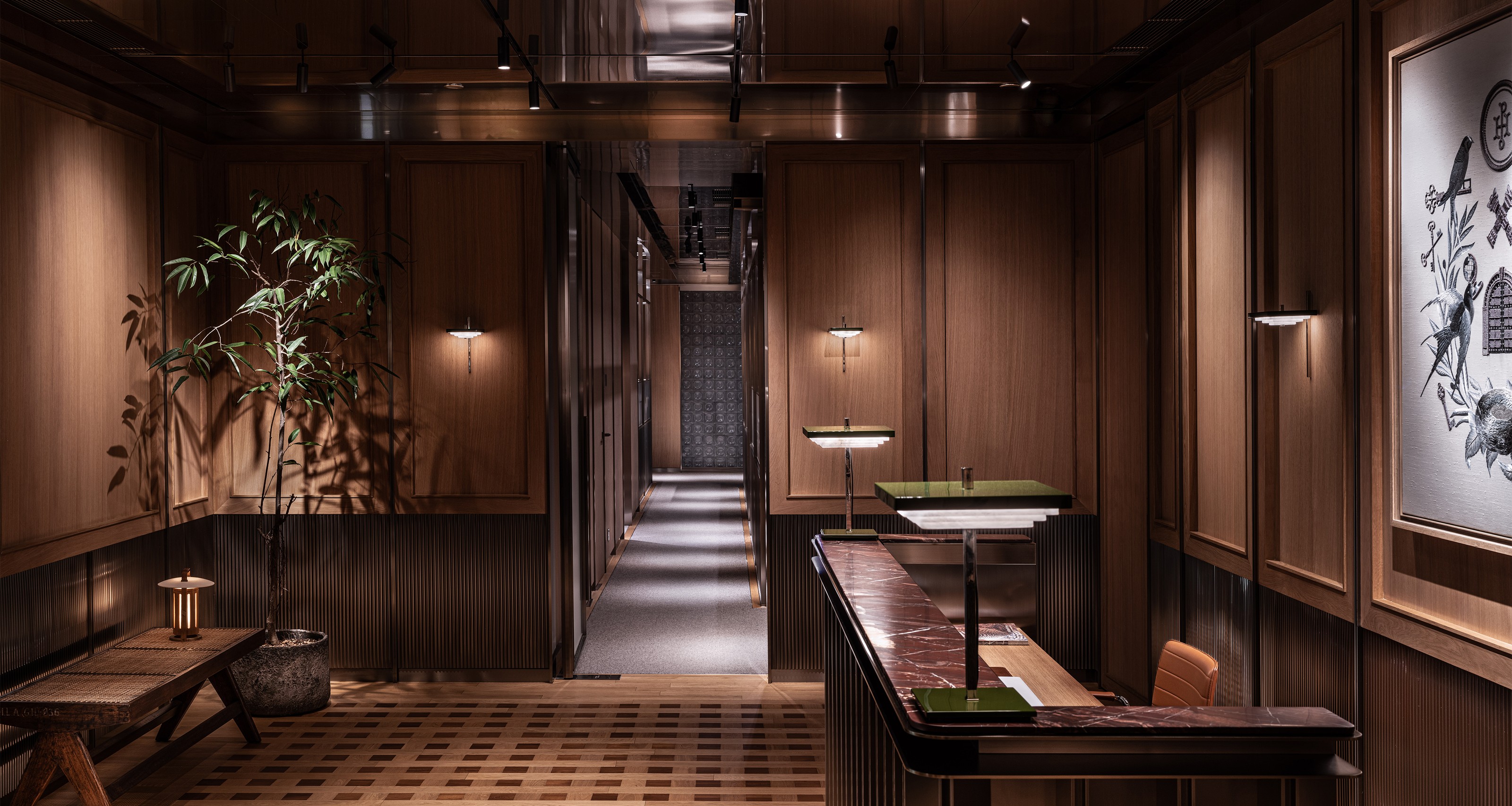 A warm, wood-paneled reception area with a marble-topped desk, a potted plant, and a long hallway.