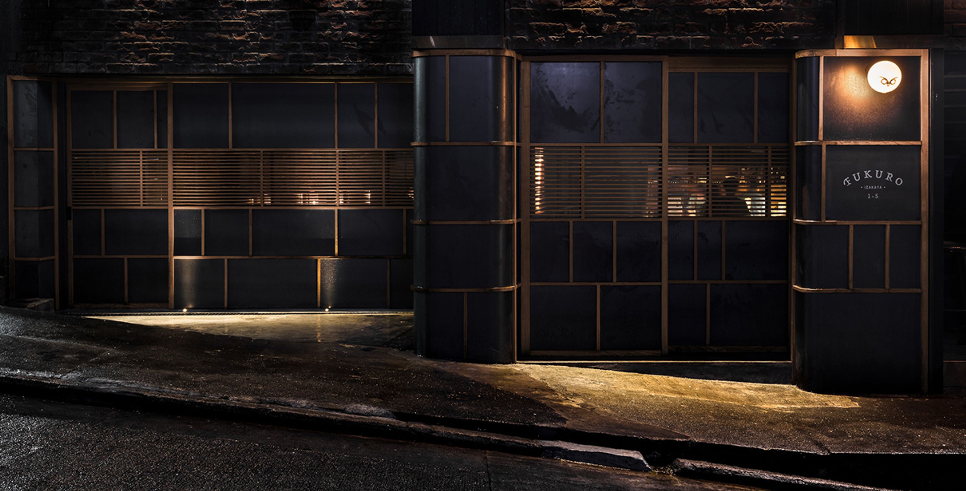 Sleek dark building with gold-trimmed panels and a 'MUKURO' sign, illuminated at night.