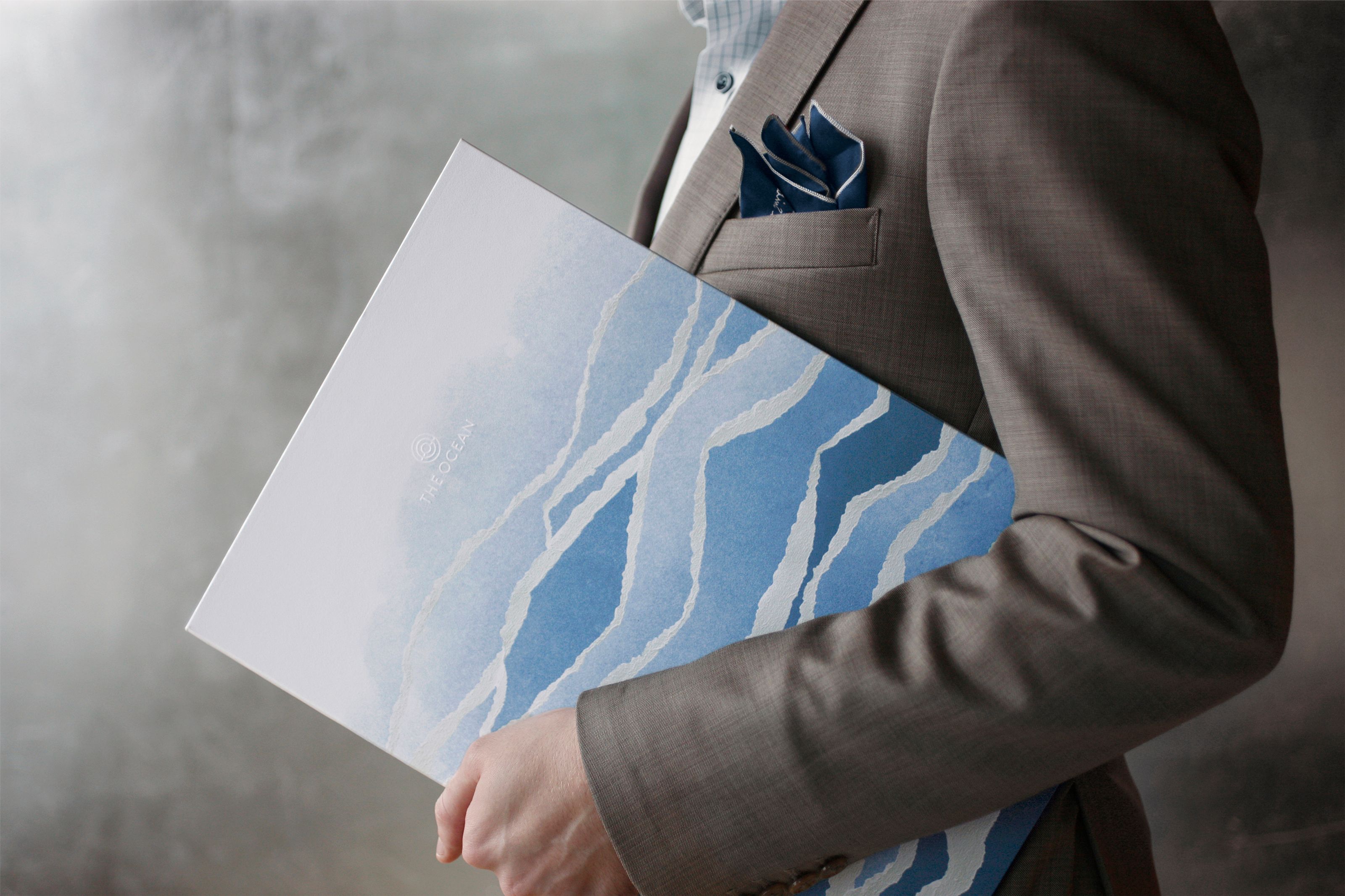 Person in a suit holding a brochure with blue wave patterns and 'THE OCEAN' text.