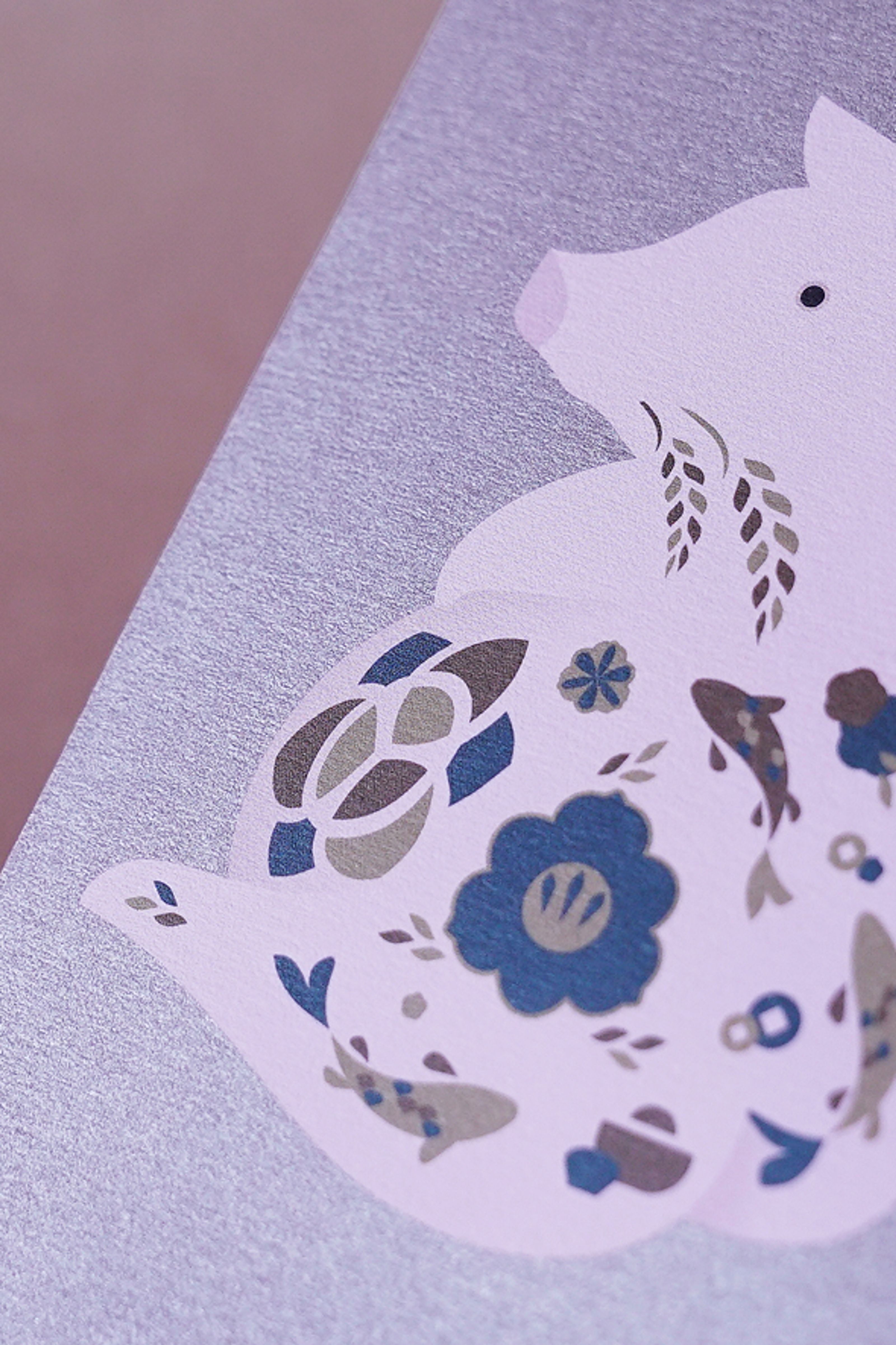 Close-up of a pale purple pig illustration featuring blue, grey, and brown floral and fish patterns, on a textured light purple background.