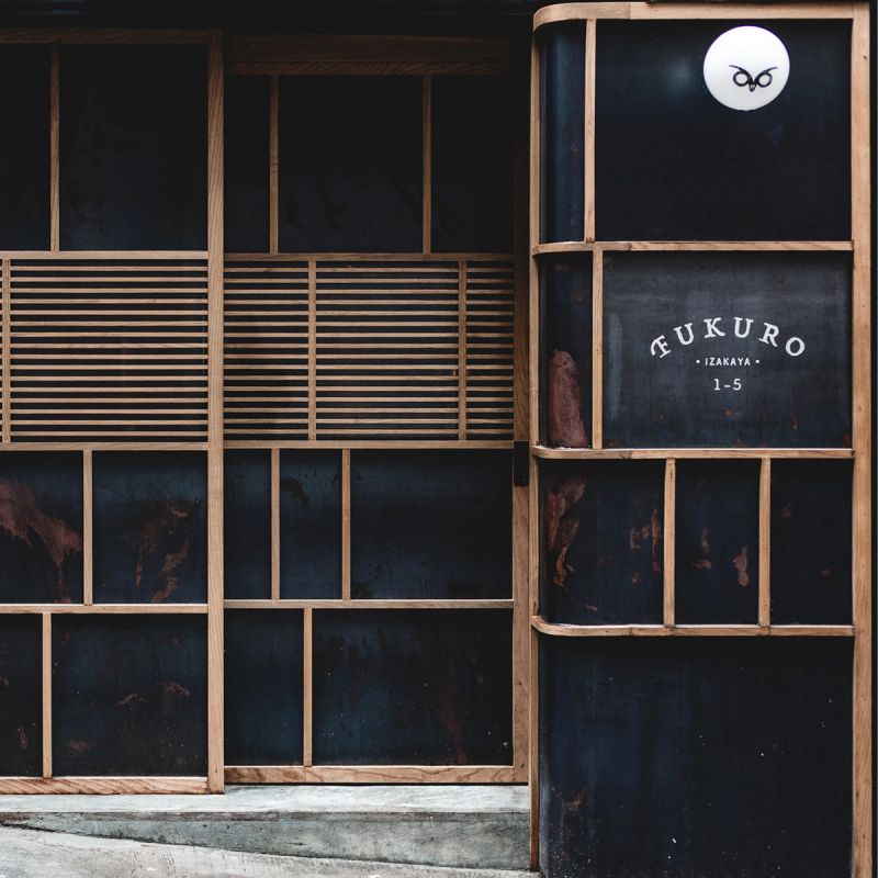 Dark, wood-framed storefront with an open door displaying "FUKURO IZAKAYA" text and an owl logo.