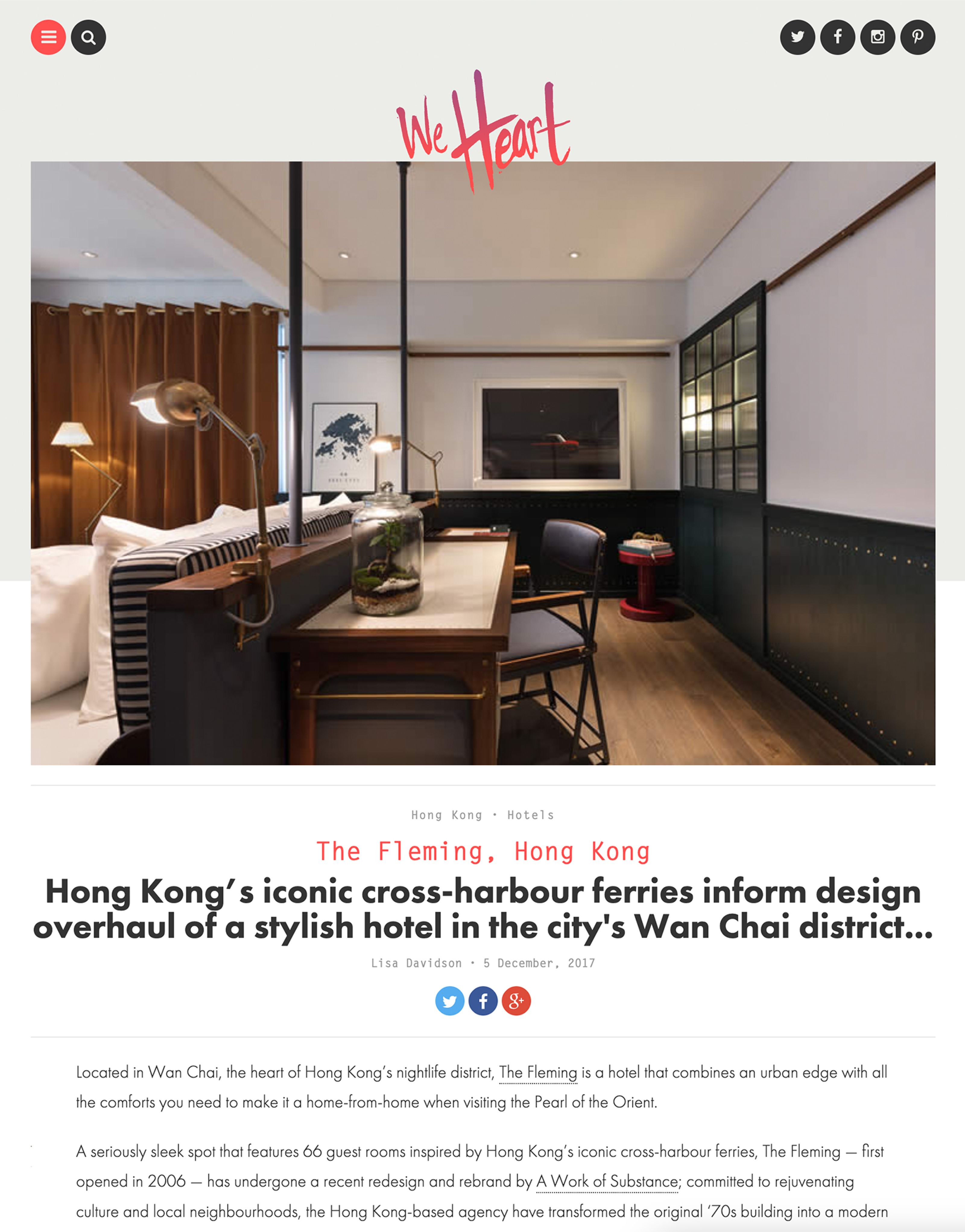A stylish hotel room featuring a long desk with two brass lamps, a terrarium, and dark industrial-style panels.