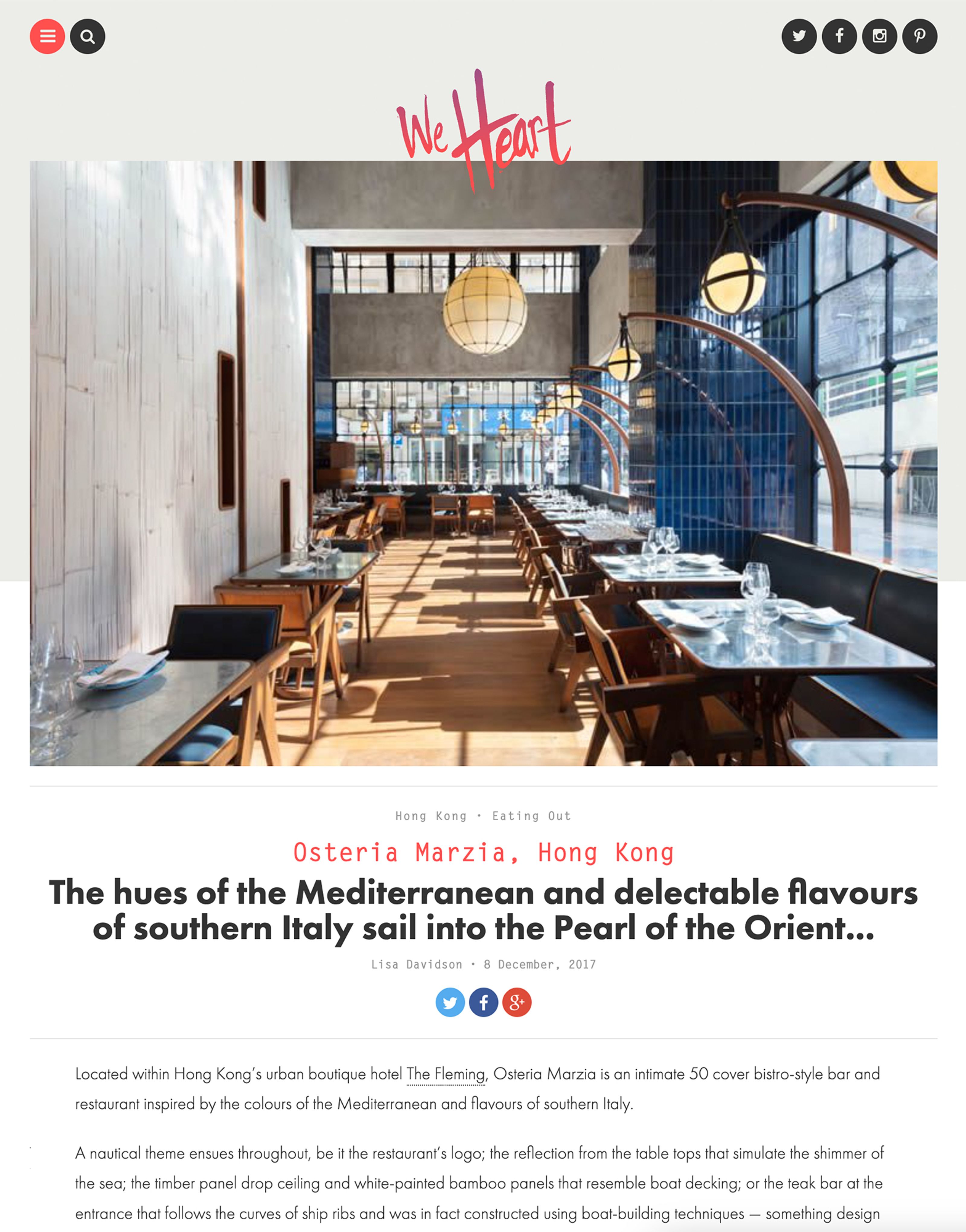 A modern restaurant interior with long rows of dining tables, wooden chairs, spherical pendant lights, and a blue tiled wall next to large windows.