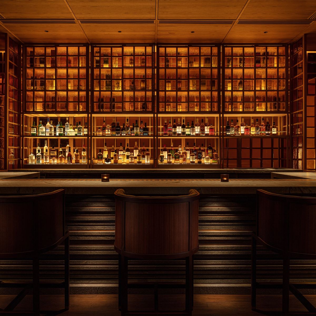 A warmly lit bar with shelves of liquor bottles and two bar stools.