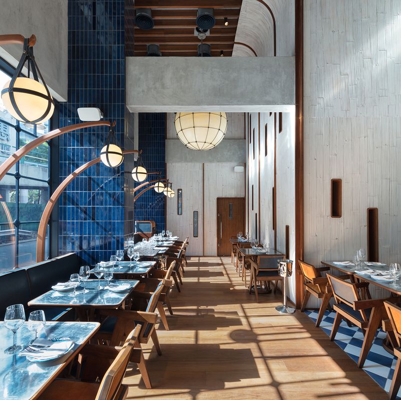 A modern restaurant interior featuring a dark blue tiled wall, textured light wood panels, and unique spherical pendant lights over set dining tables.