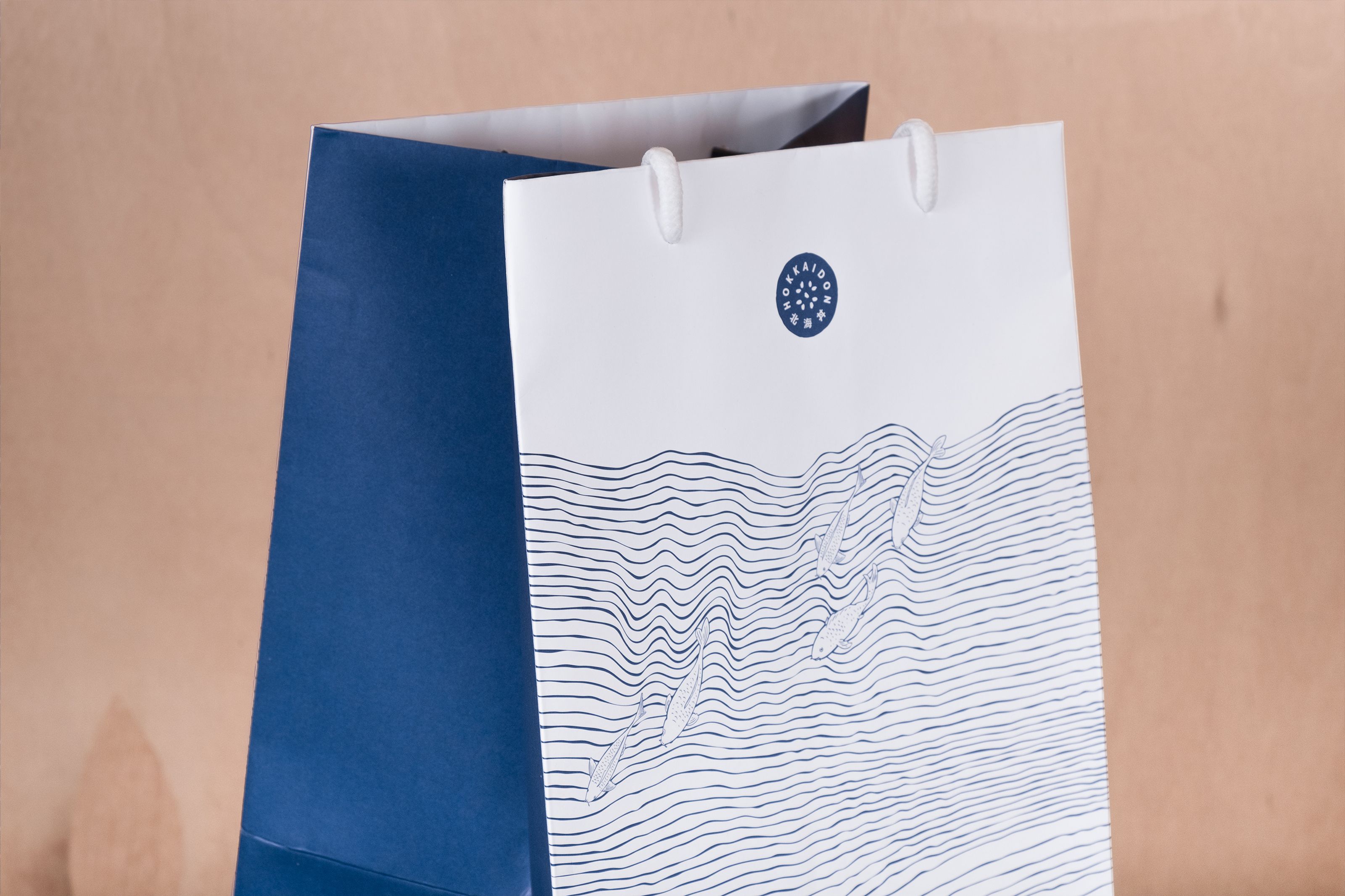 White and dark blue gift bag with a nautical design featuring a circular logo, wavy lines, and fish.