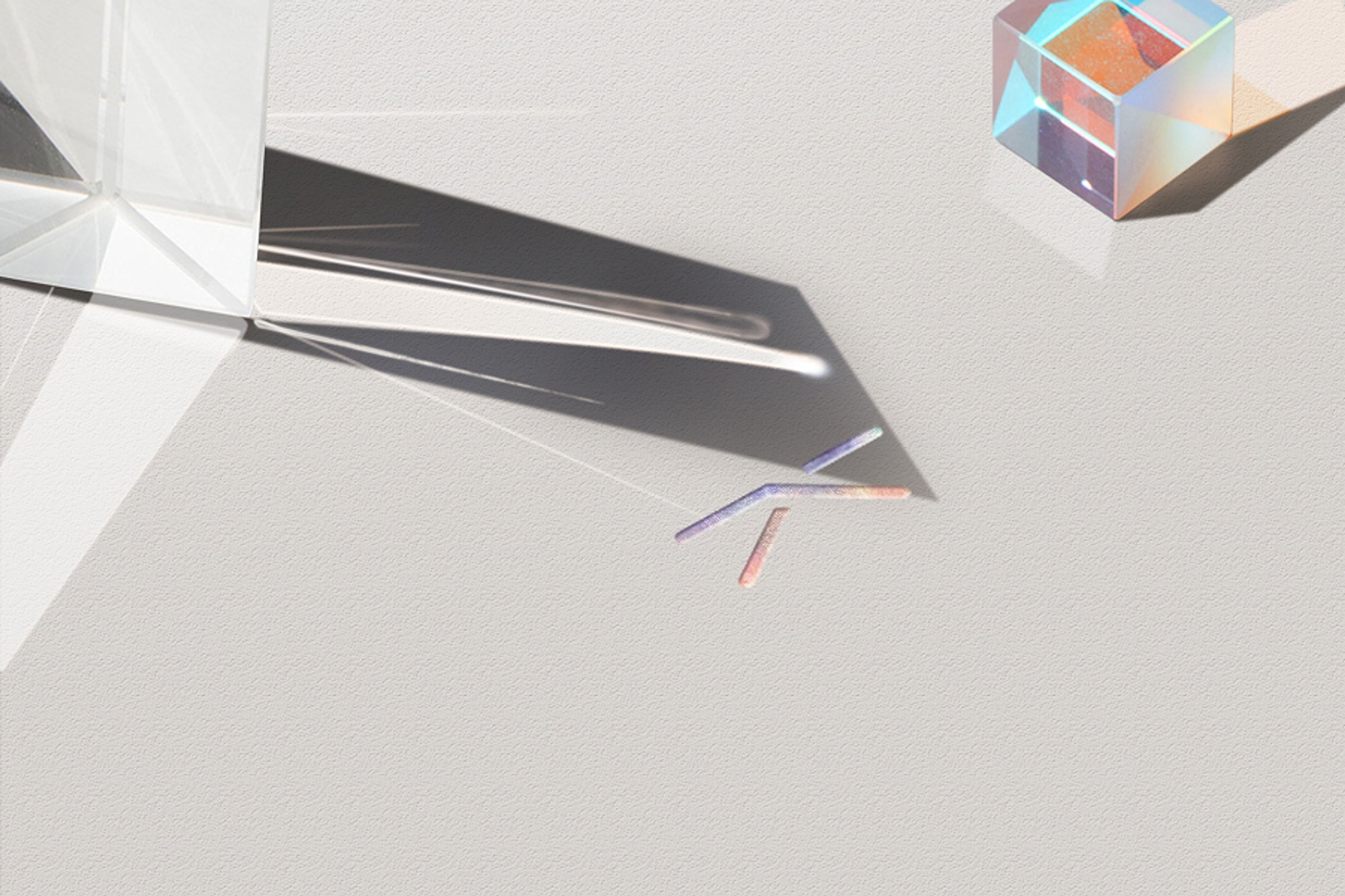 A clear prism and a dichroic cube prism on a light gray surface, creating colorful light refractions and shadows.