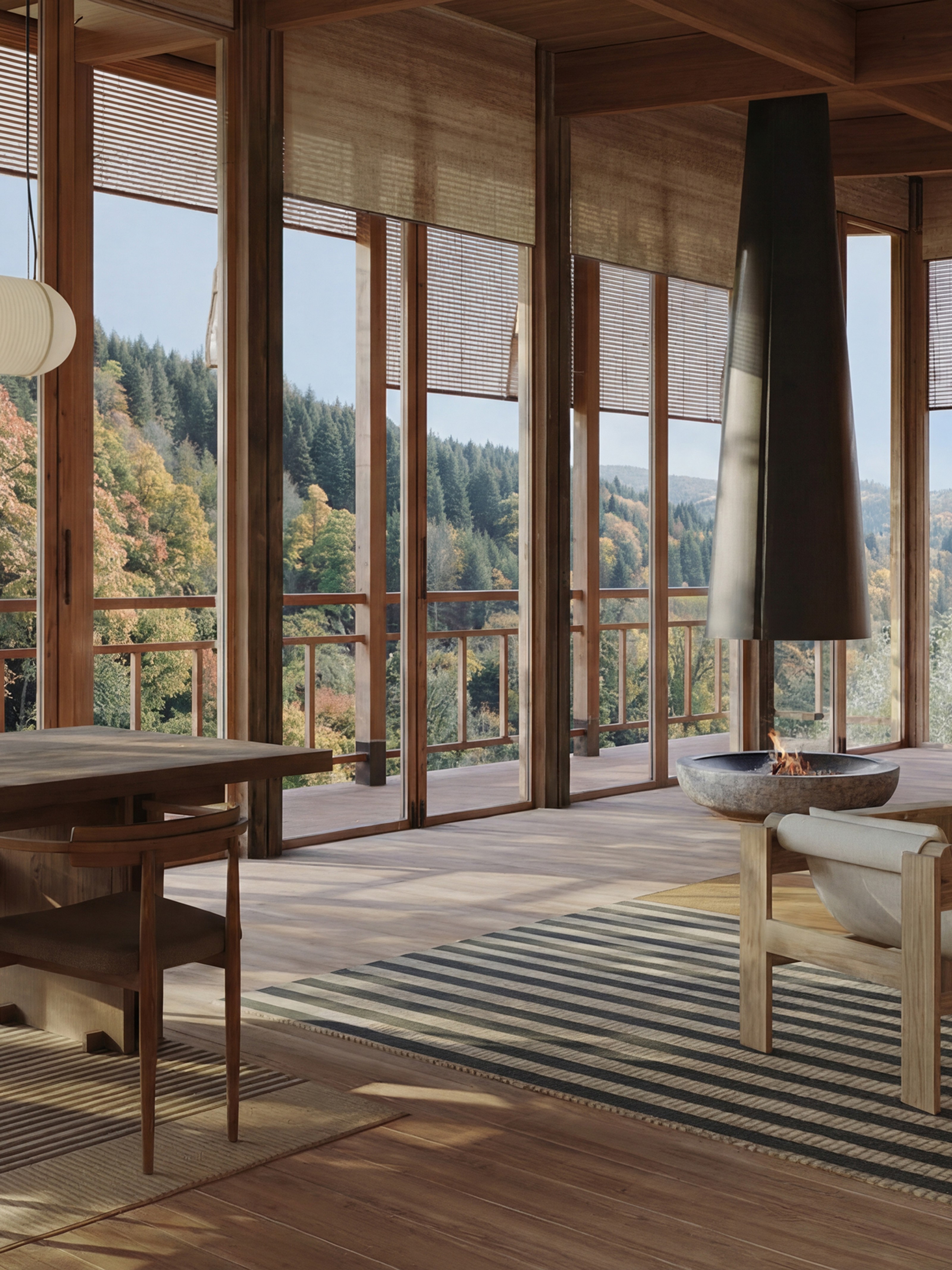 Modern wooden interior with full-height windows offering a view of an autumn forest, featuring a dining table and a minimalist fireplace.