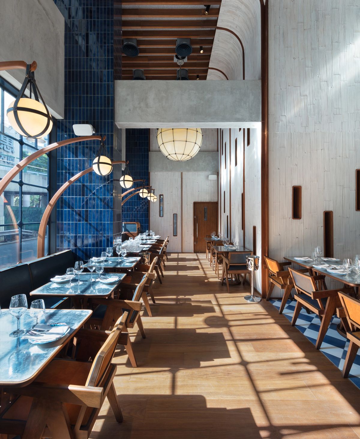 Modern restaurant interior with a blue tiled wall, textured white wall, wooden floor, and dining tables with unique hanging globe lights.