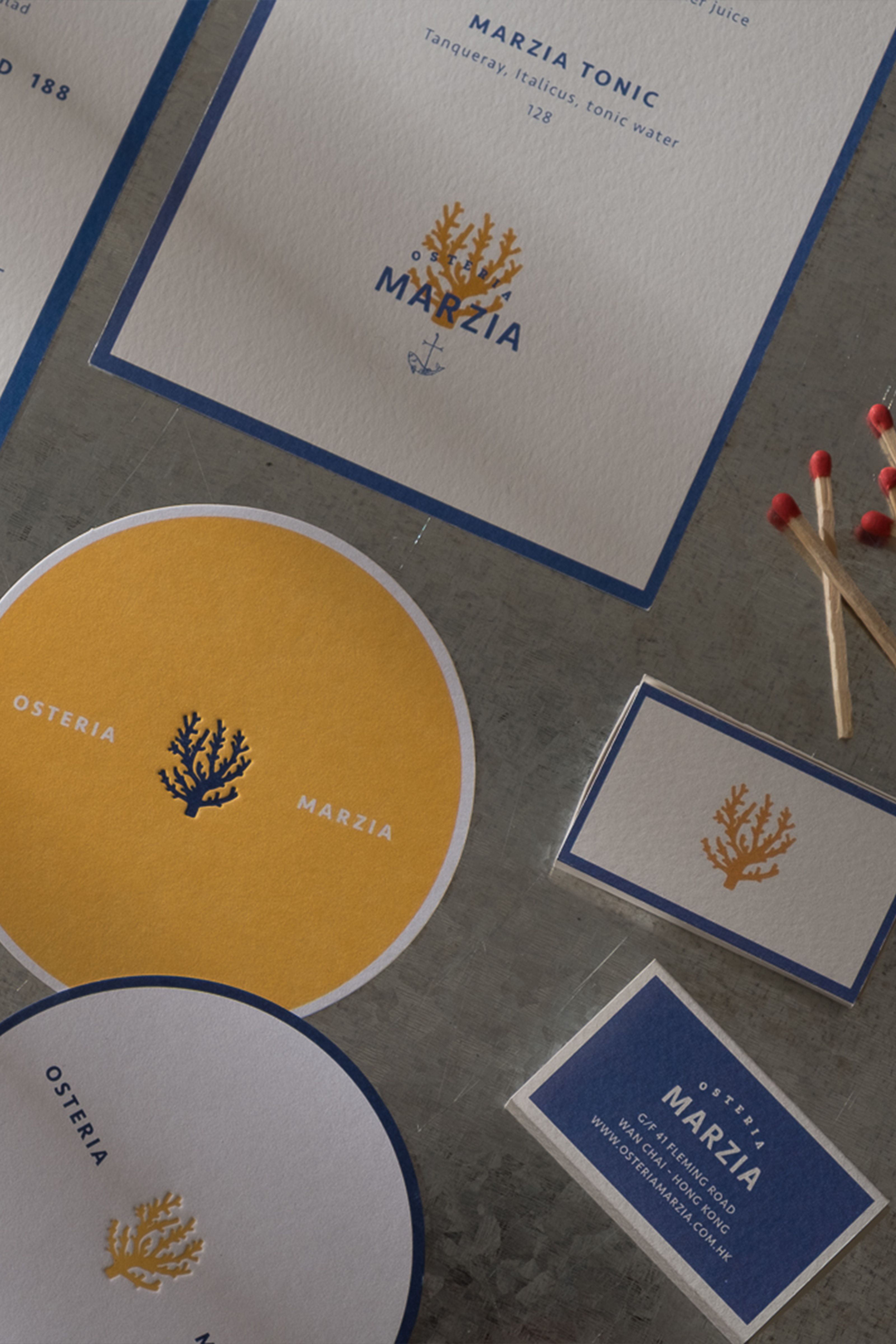 Branding for Osteria Marzia, including menus, coasters, and cards, featuring a coral logo in blue, yellow, and white, with matches nearby.