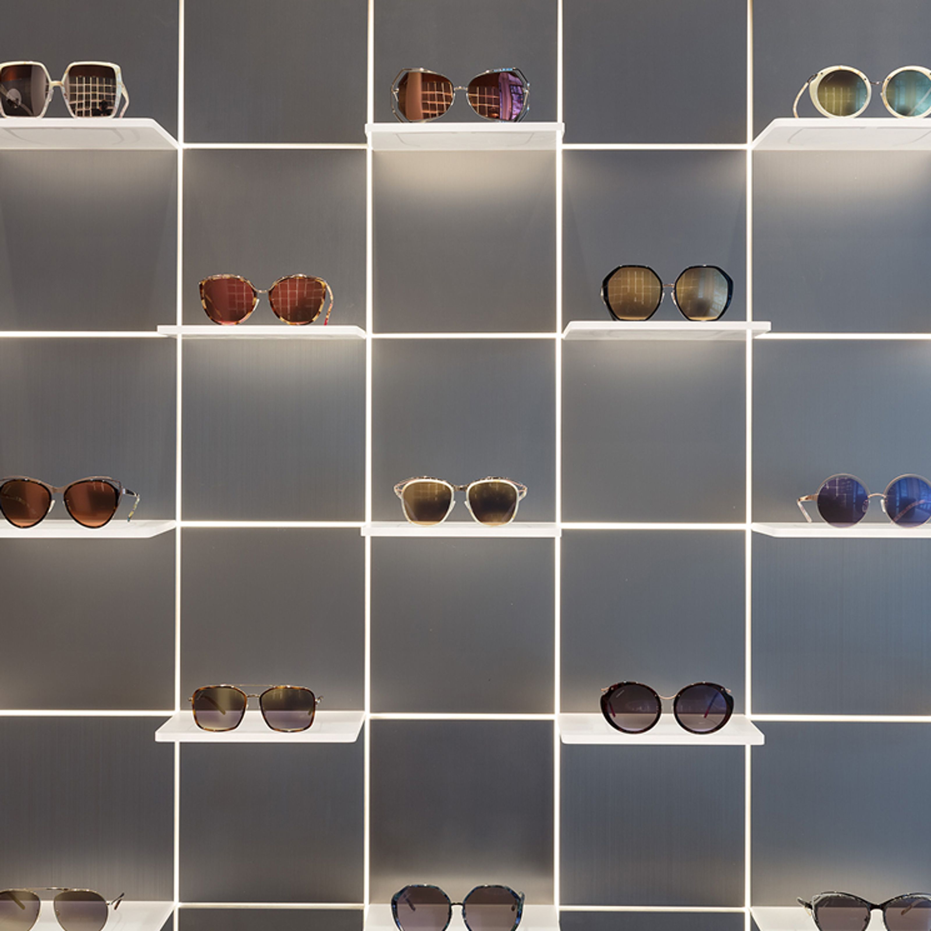 Various sunglasses displayed on illuminated grid shelves.