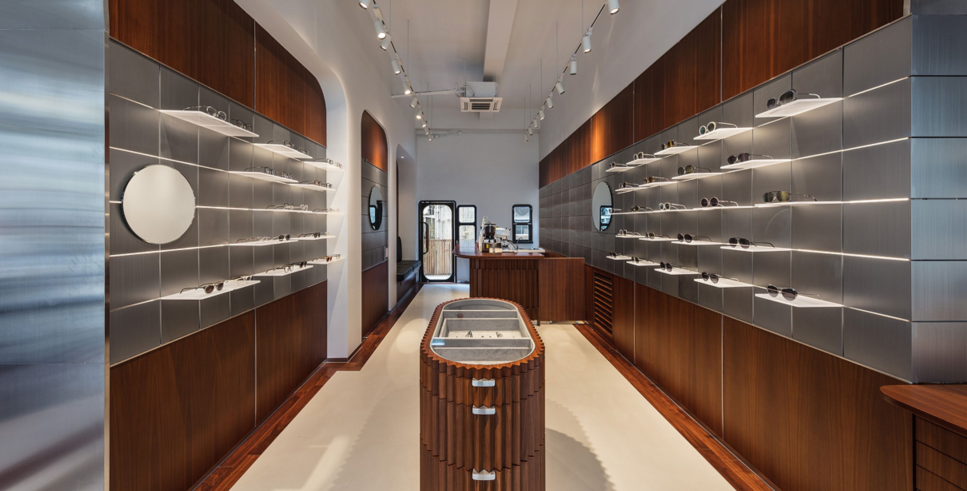 Modern eyewear store interior with wood and gray paneled walls, illuminated shelves displaying glasses, and a unique central wooden display.