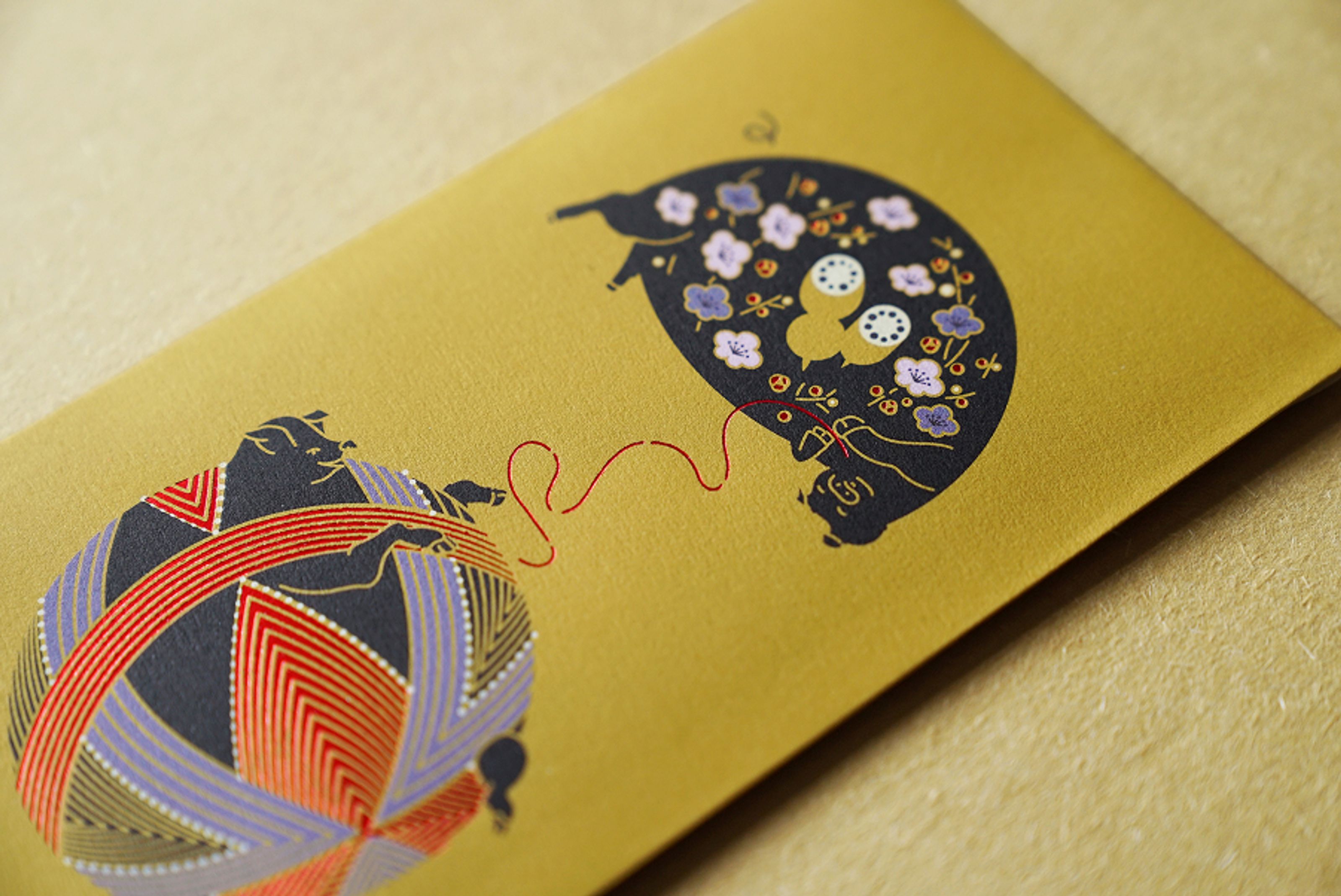 Two illustrated pigs on a gold background, one holding a patterned yarn ball, the other sewing a floral design, connected by a red thread.