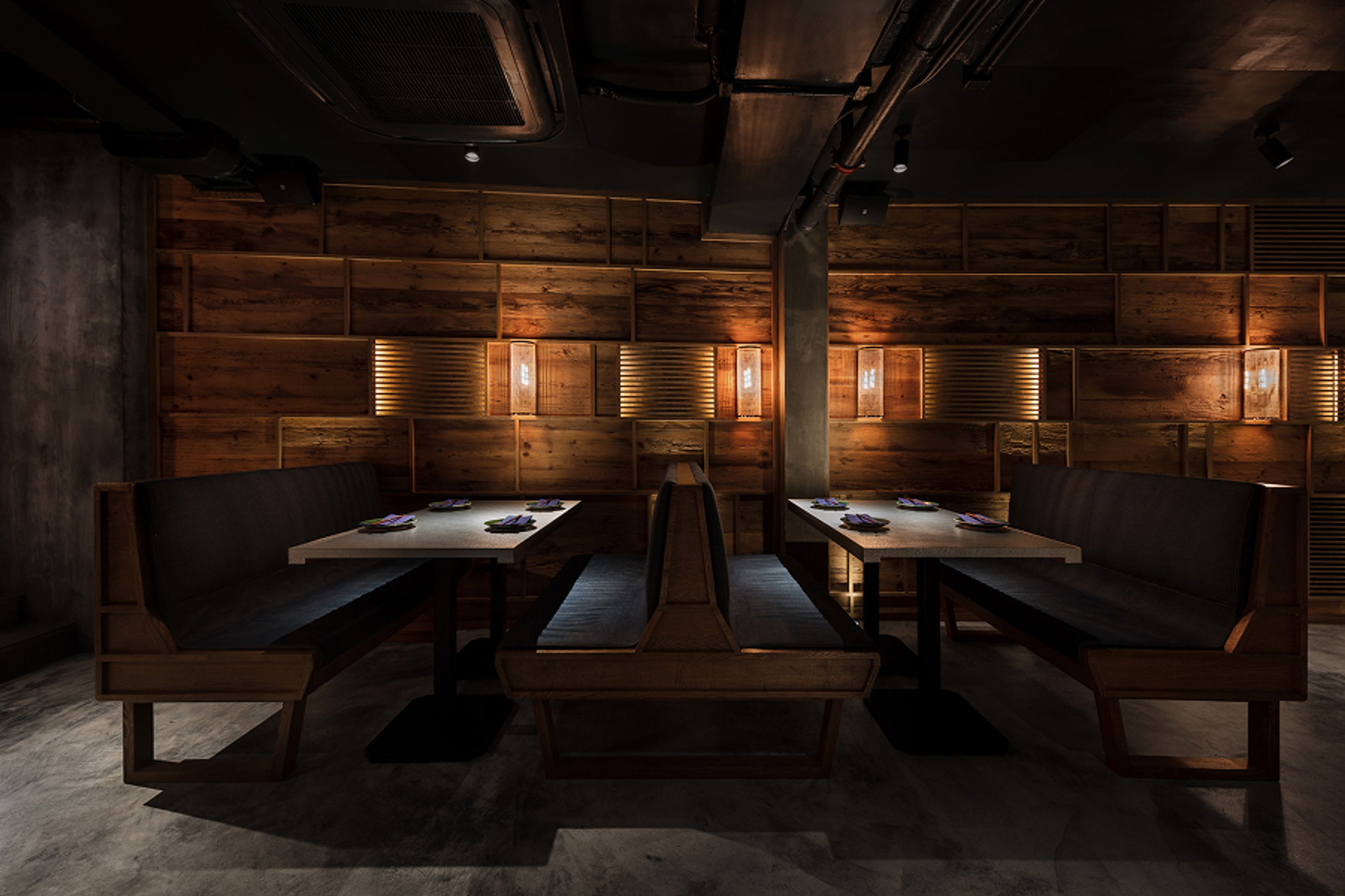 Modern restaurant interior with dark wood panel walls, subtle lighting, two booth tables, and purple plates.