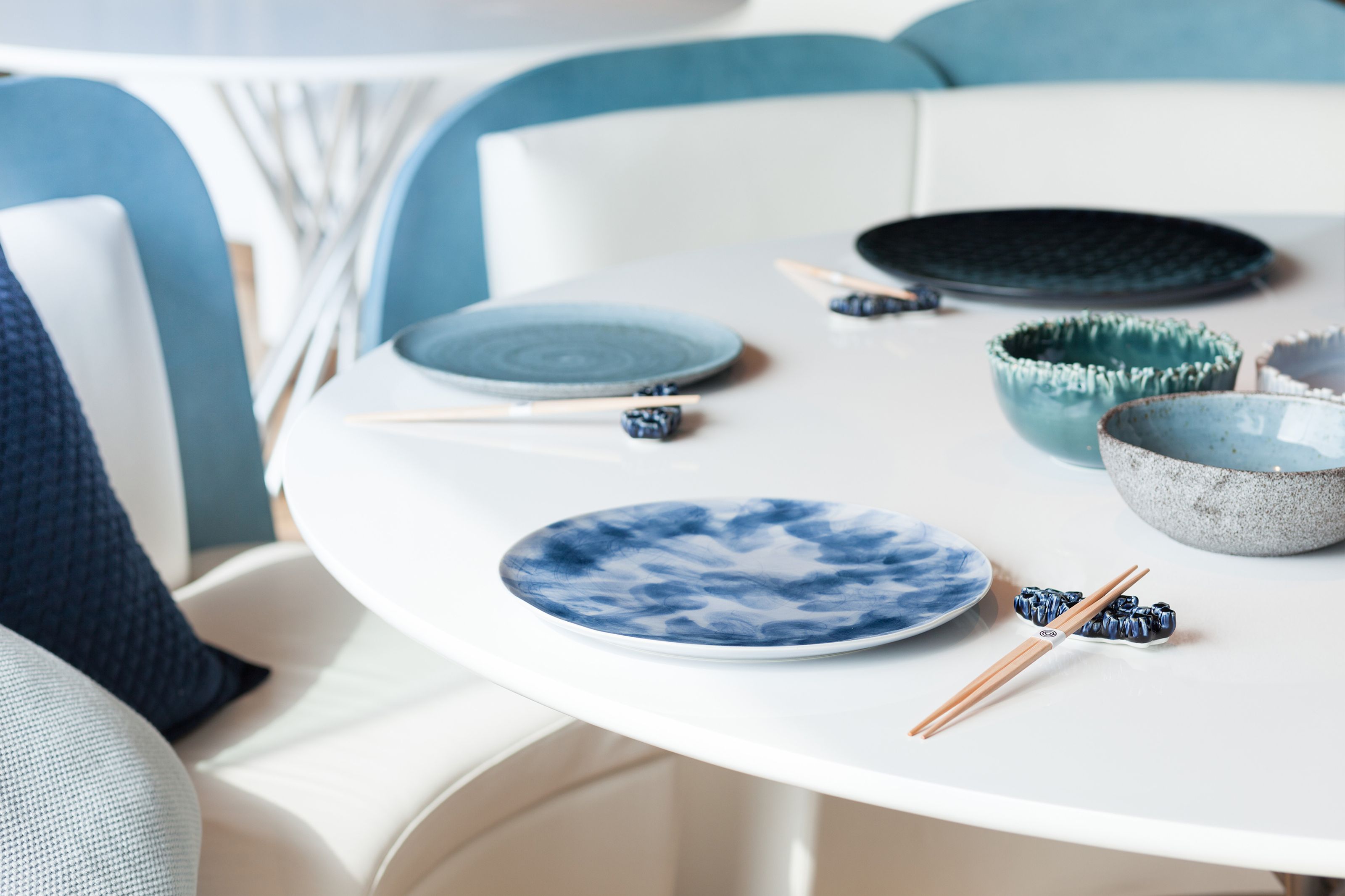 White table set with blue and grey ceramic dishes and chopsticks, against a backdrop of blue and white seating.