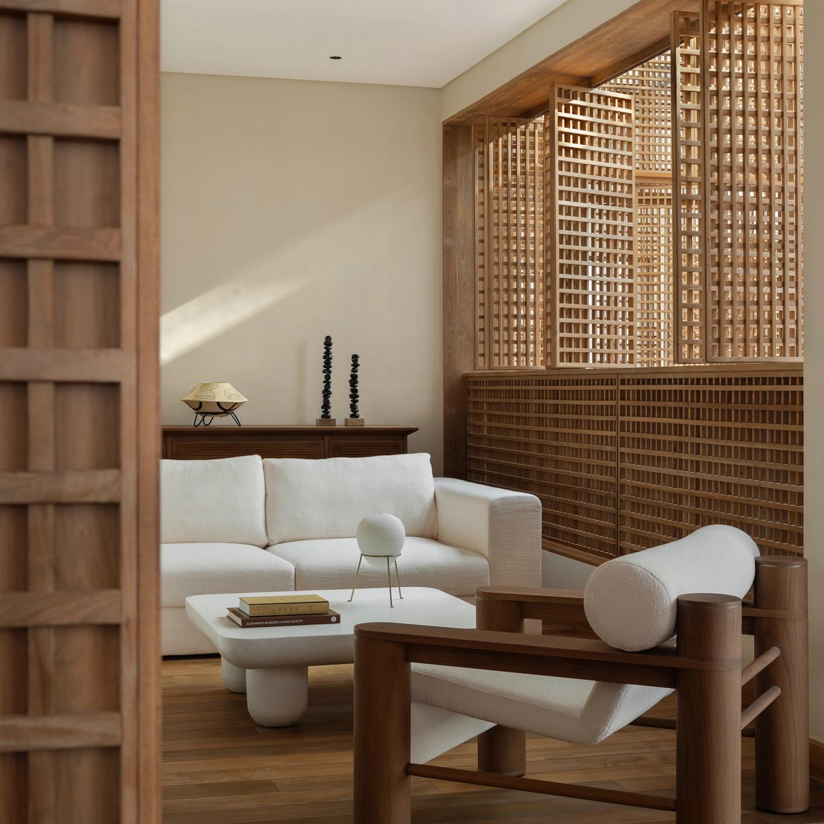 A modern living room with a white sofa, a white coffee table, and a wooden armchair, featuring large wooden lattice screens on the back wall.