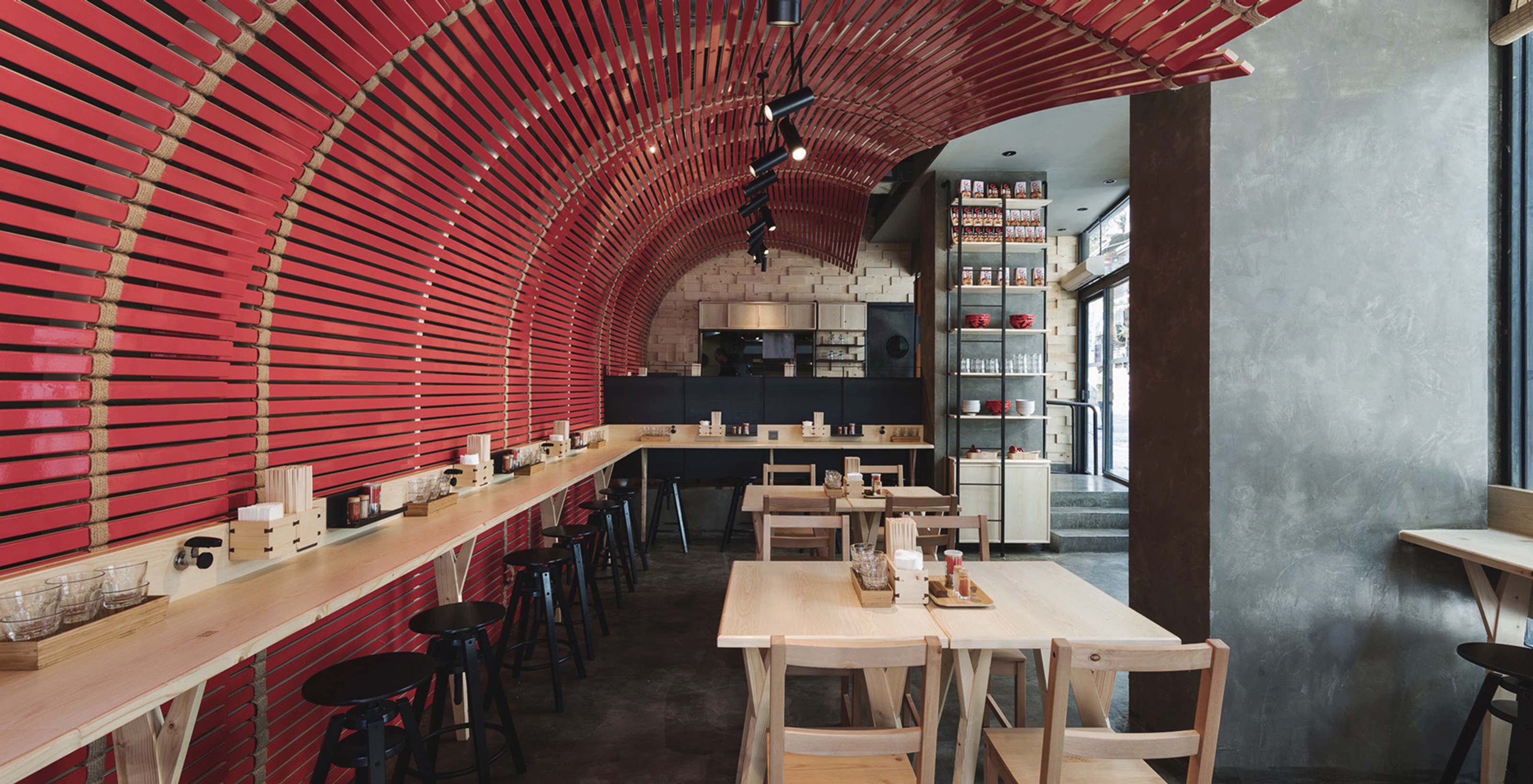 Modern restaurant interior with a striking red slatted arched ceiling, light wood counter seating, and tables.