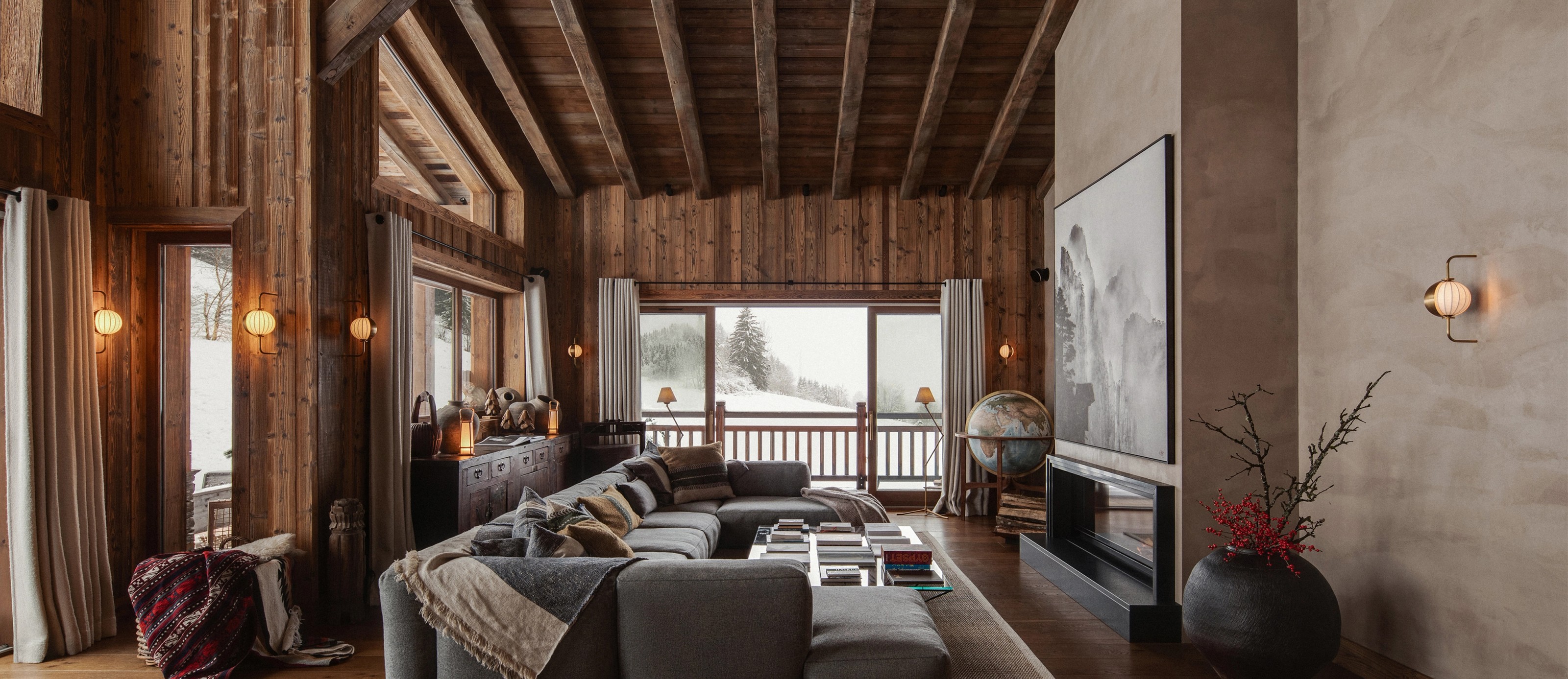 Luxurious ski chalet living room with wooden walls, a large sectional sofa, fireplace, and snowy mountain view.