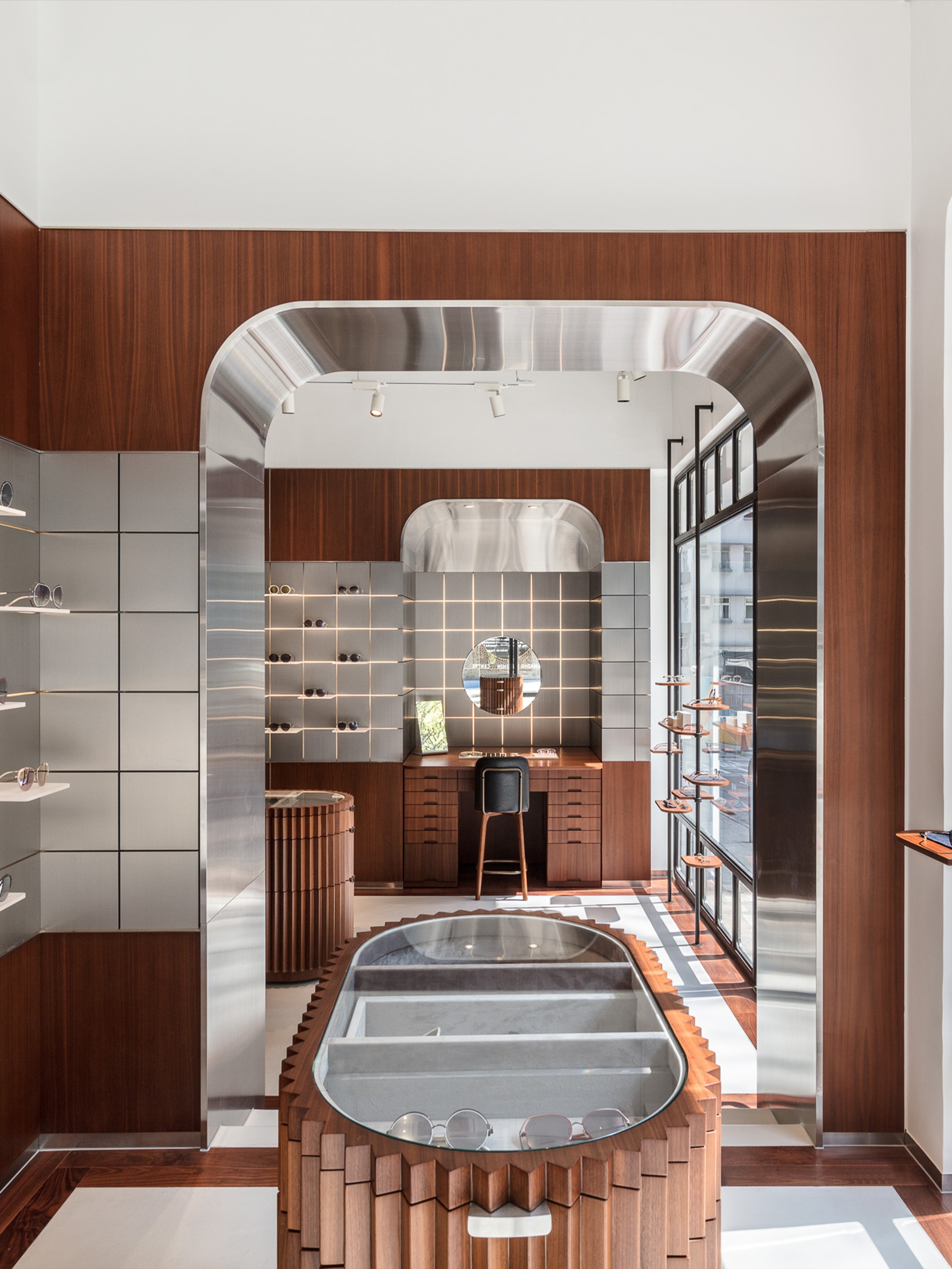 Modern optical store interior with wood paneling, sleek metallic arches, and multiple eyeglasses displays.