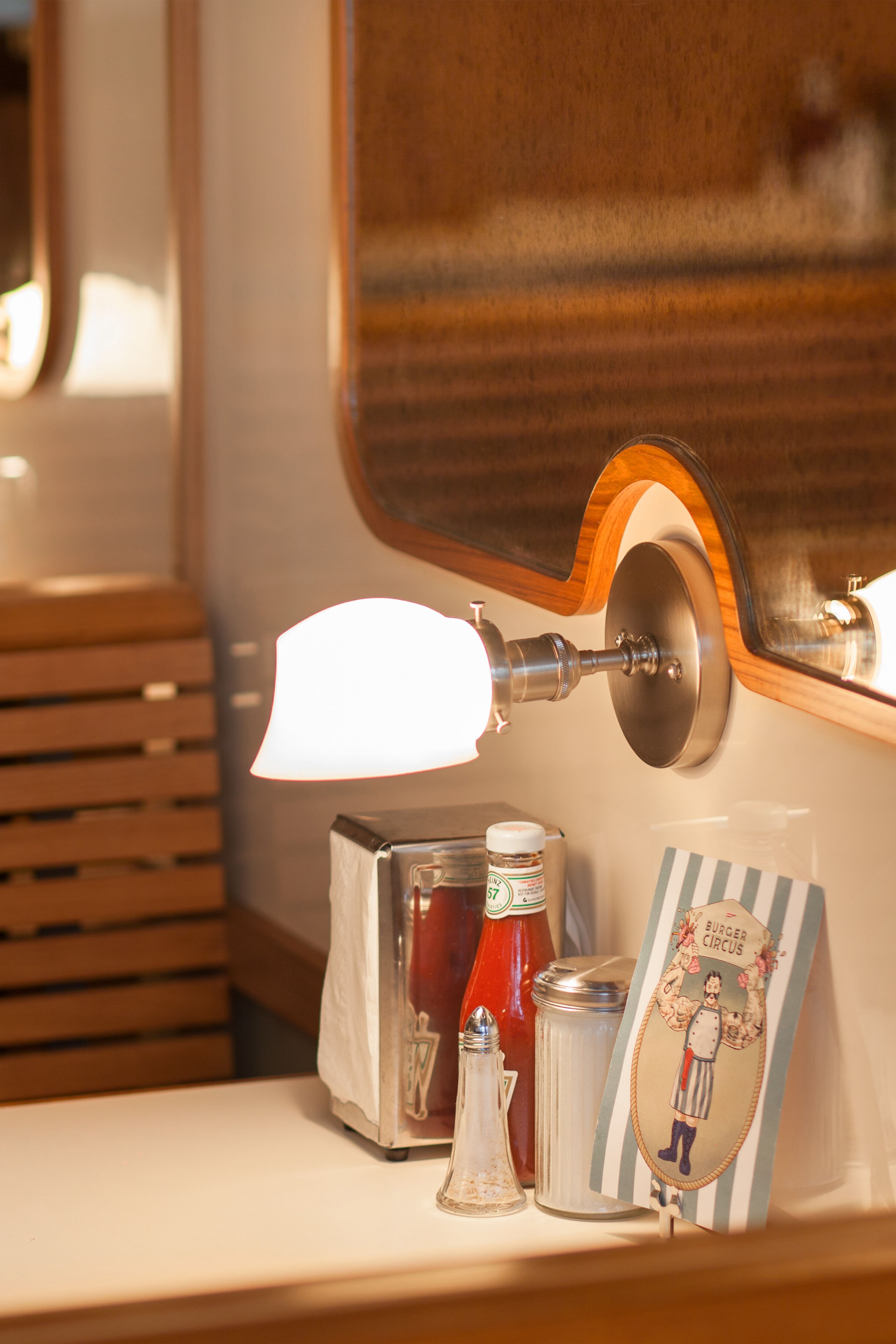 A brightly lit diner table setting with a napkin dispenser, ketchup, salt shaker, sugar dispenser, and a "Burger Circus" menu.